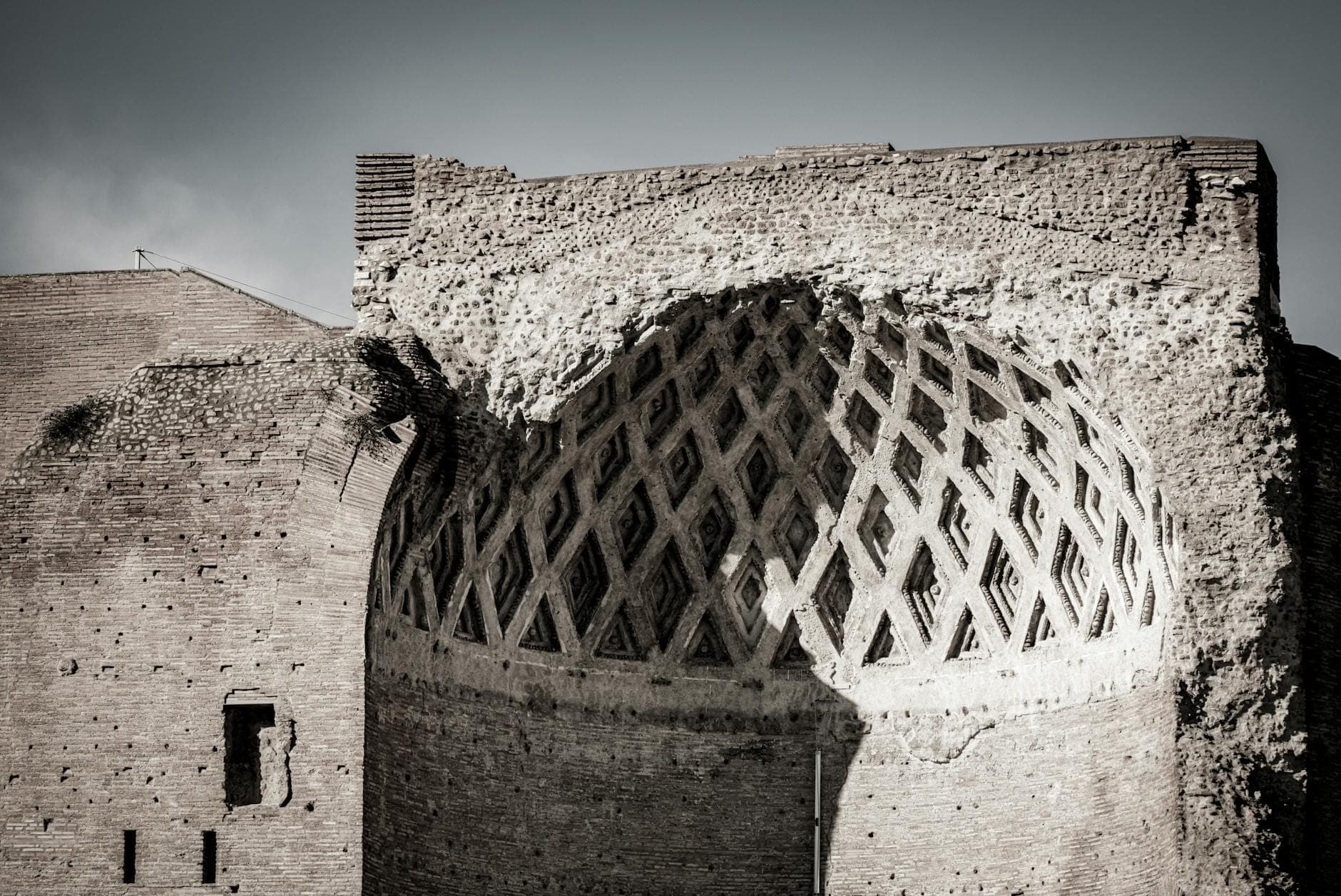 Primo piano di un antico muro in mattoni e di un soffitto a volta parzialmente crollato nella Domus Aurea, che mette in risalto i motivi architettonici romani sotto un cielo sereno.