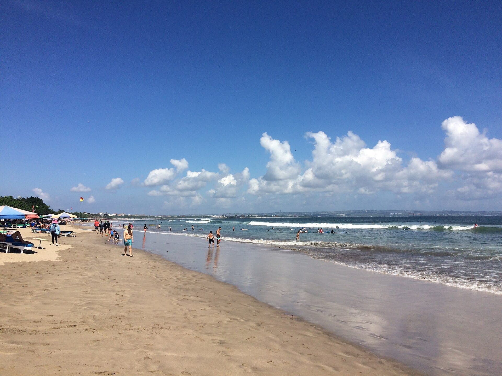 Wide white sands of Double Six Beach in Seminyak with umbrellas, and gentle waves lapping the shore.