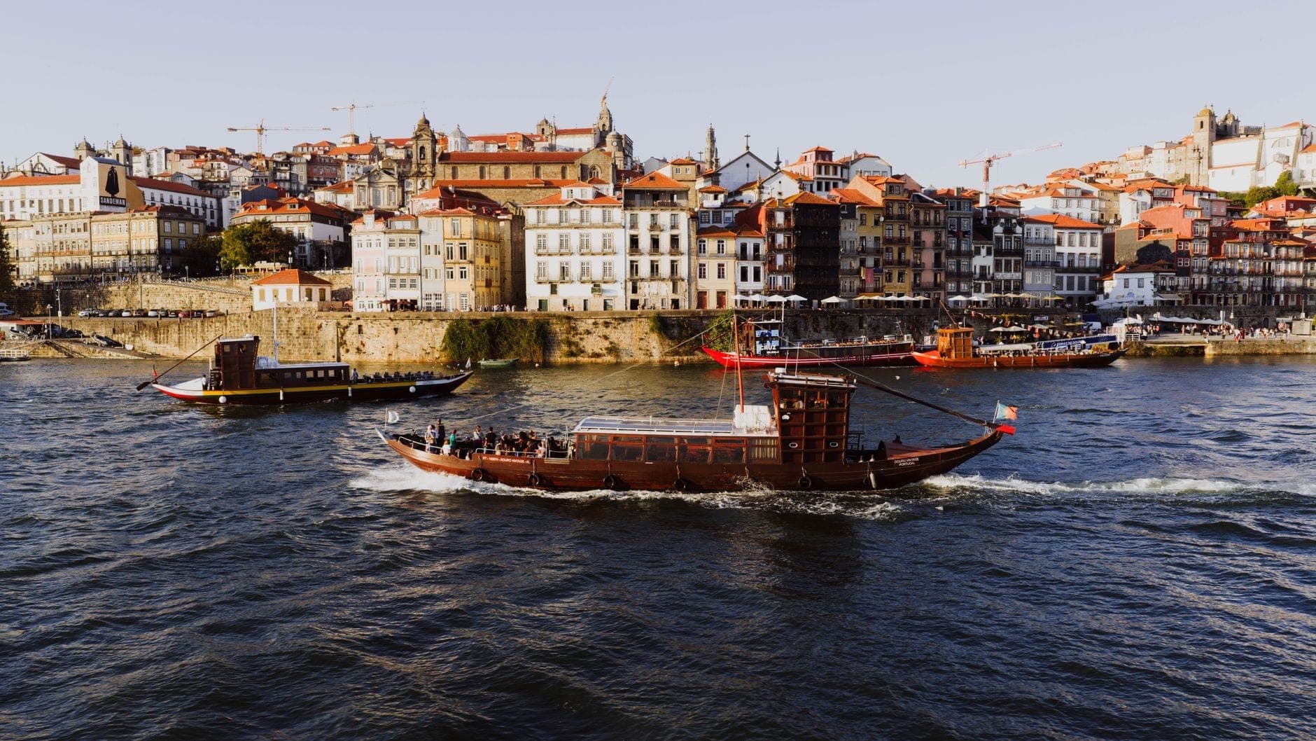 Traditionelles Boot auf dem Douro mit Portos bunten historischen Häusern und der Skyline im Hintergrund an einem sonnigen Tag.