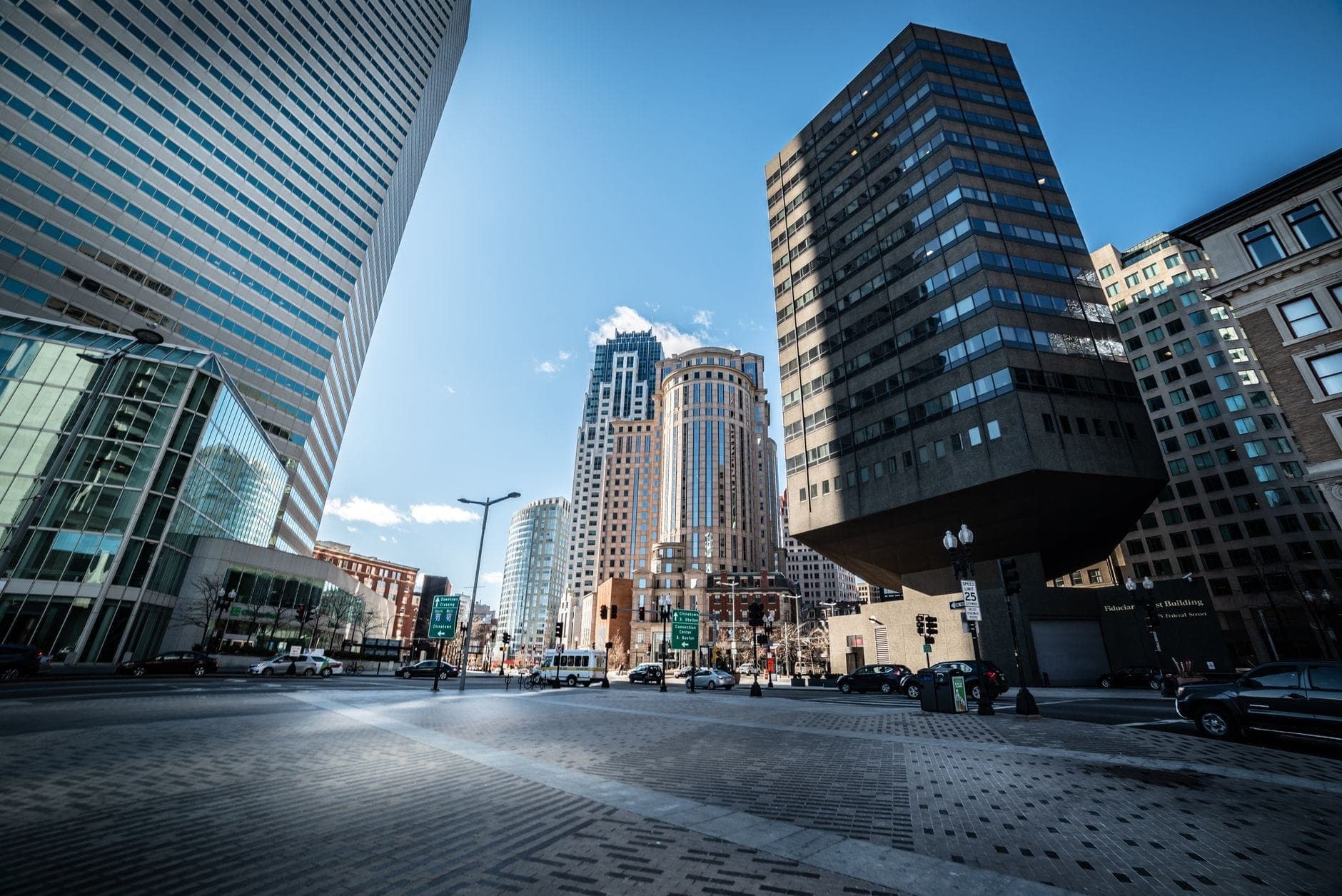 Vue panoramique du Financial District de Boston avec ses gratte-ciel en verre, ses immeubles anciens, une rue animée et un ciel d'un bleu éclatant, reflet du dynamisme urbain de la ville.