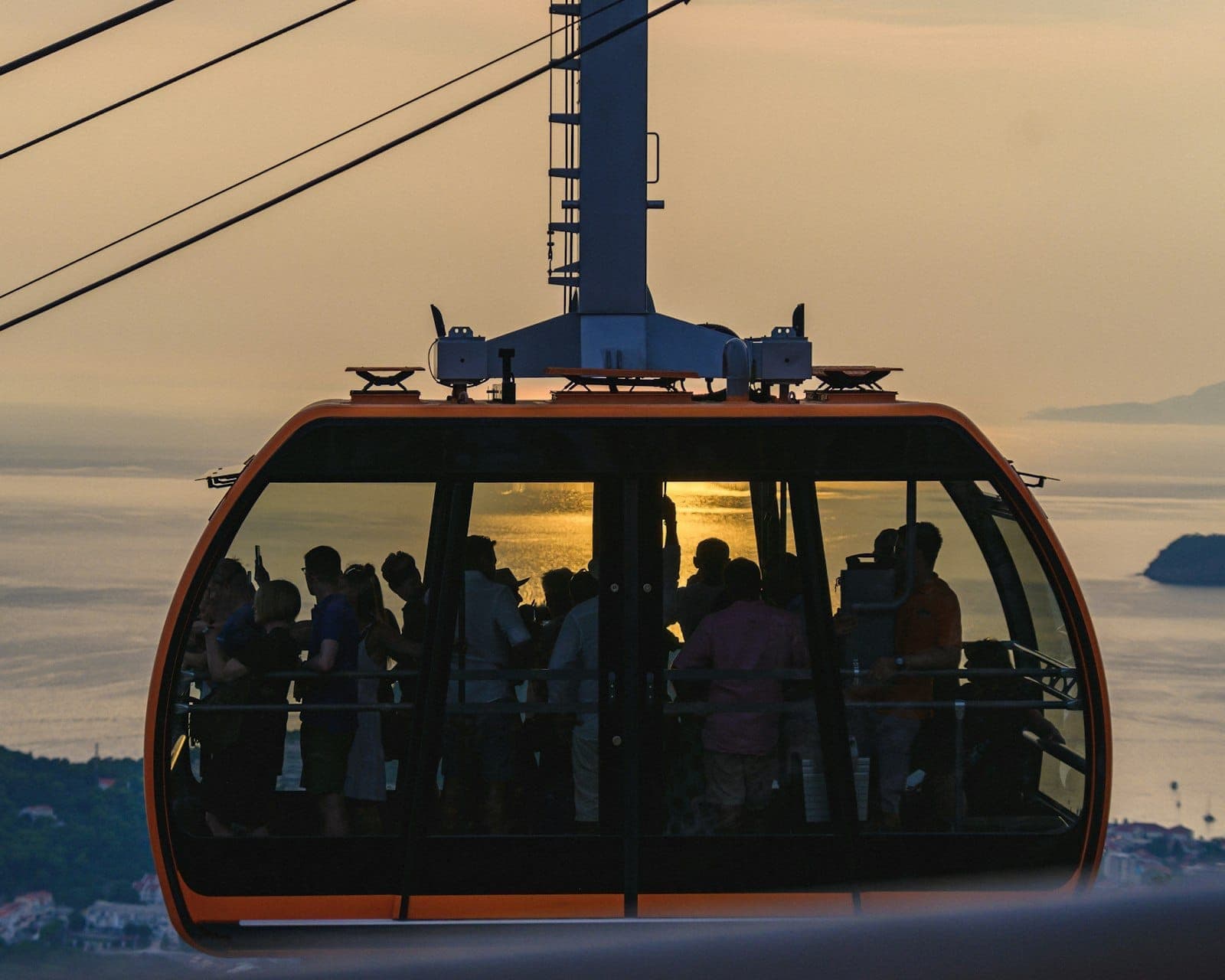 Close do teleférico de Dubrovnik lotado de pessoas ao pôr do sol, cabos aéreos e mar Adriático ao fundo.