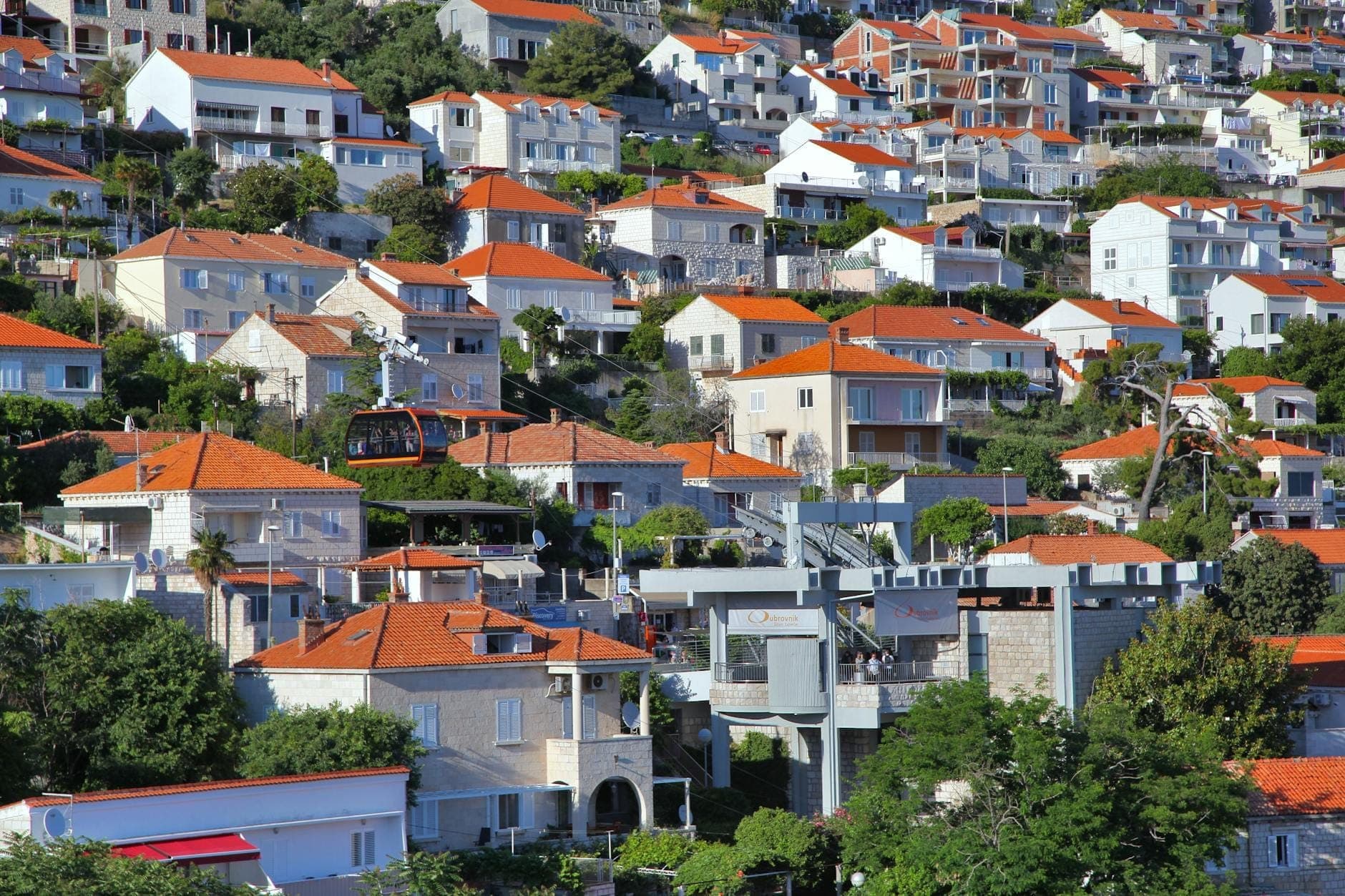 Conjunto de casas de Dubrovnik com telhados laranja e teleférico passando por área residencial a caminho da estação inferior