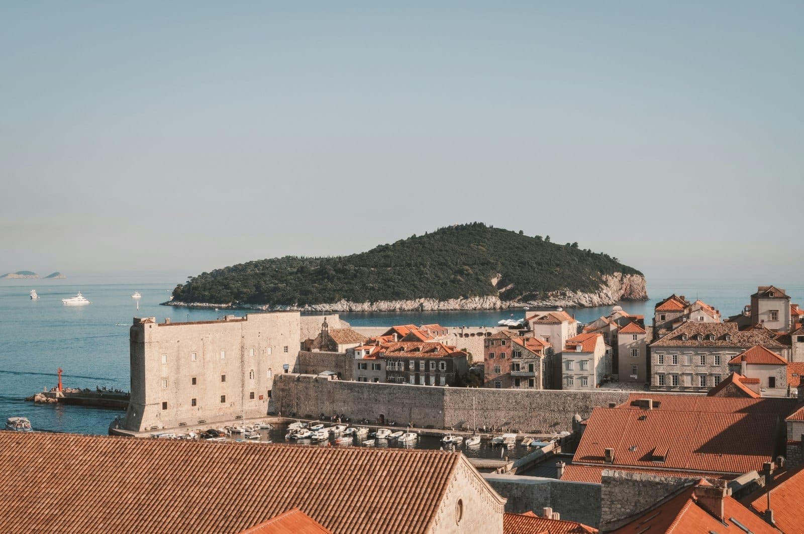Blick auf die Altstadt von Dubrovnik mit der Insel Lokrum im Hintergrund, über das Meer unter klarem Himmel gesehen.