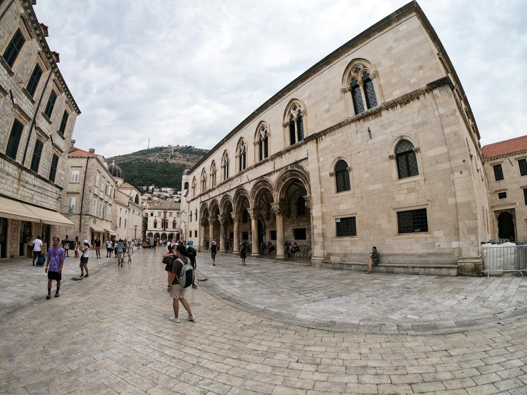 ผู้คนเดินอยู่หน้าอาคารหินประดับประดาที่มีซุ้มโค้งในเมืองเก่าของ Dubrovnik แสดงให้เห็นสถาปัตยกรรมประวัติศาสตร์ภายในกำแพงเมือง