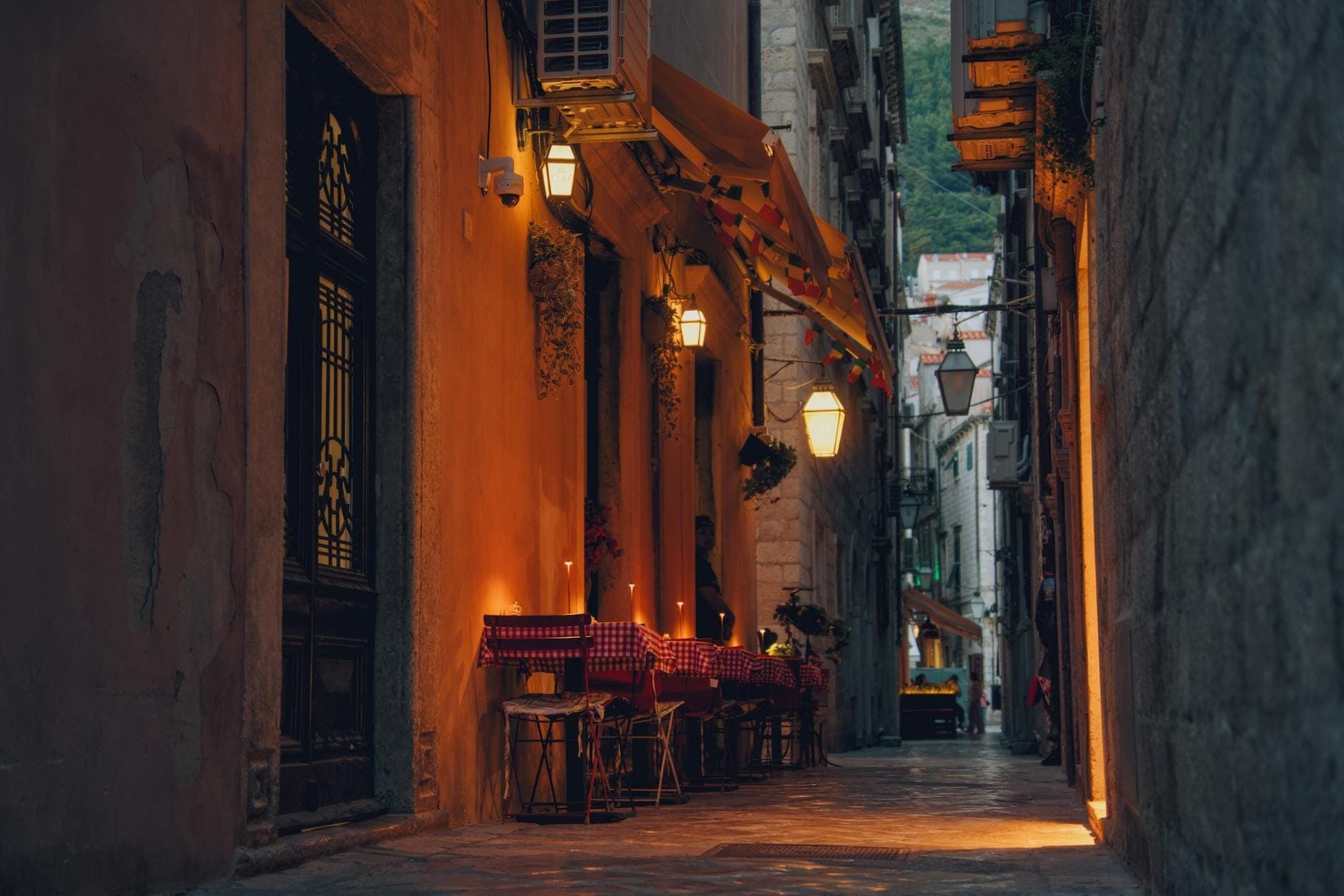Meja makan di luar ruangan dengan lilin di sepanjang gang batu tua yang sempit di Dubrovnik, menciptakan suasana makan malam yang intim dan romantis.