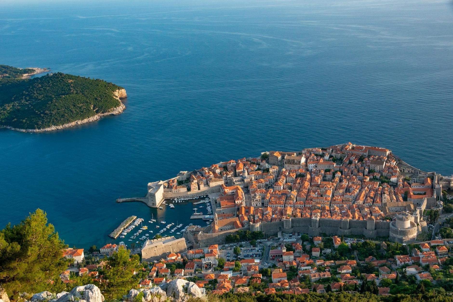 Pemandangan panoramik atas Kota Tua bertembok Dubrovnik, menampilkan bangunan bersejarah dari batu kapur, atap merah, dan Laut Adriatik yang biru tua.