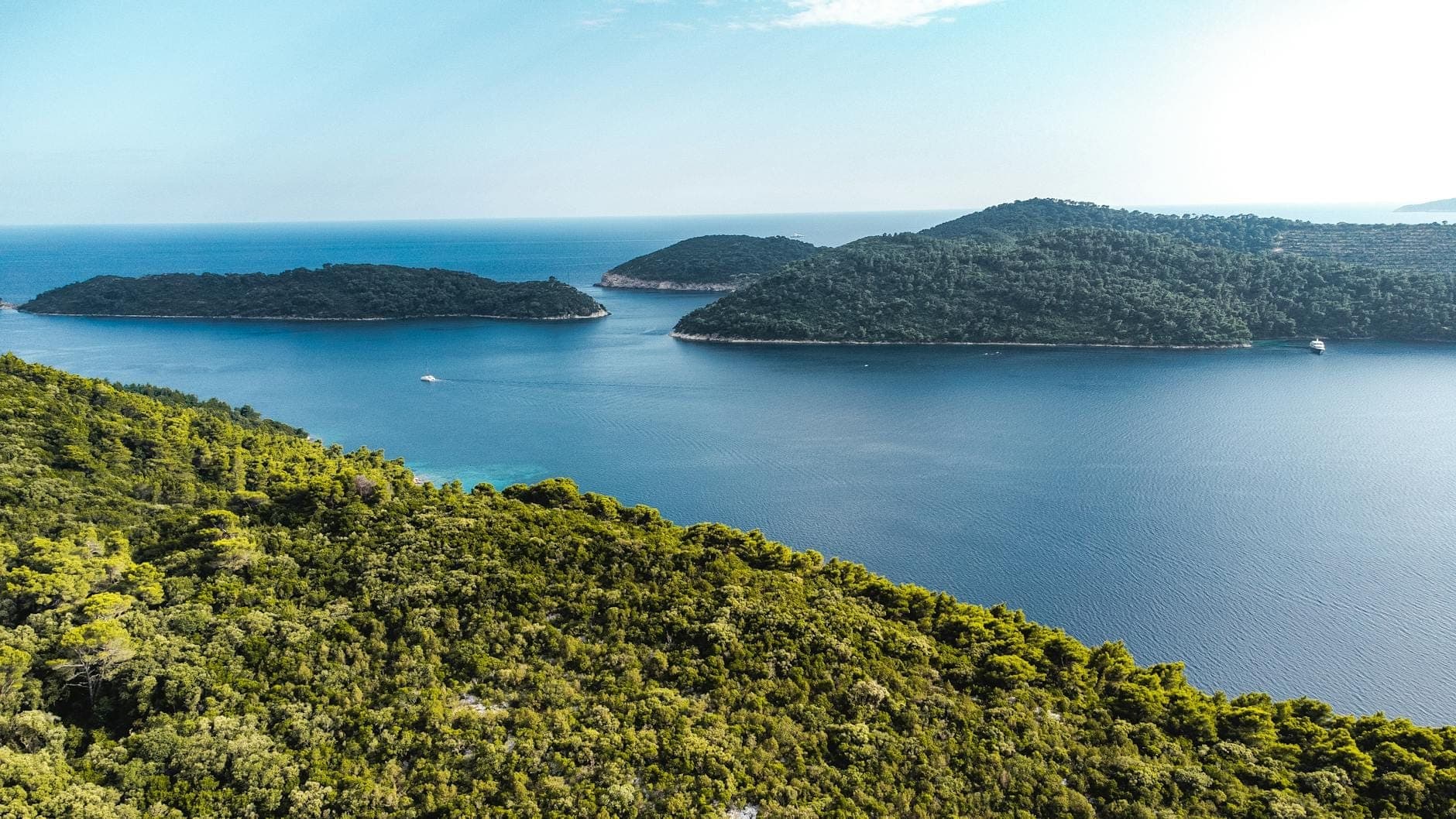Luftaufnahme von drei üppig grünen Inseln, umgeben von klarem blauem Meer in der Nähe von Dubrovnik unter einem strahlenden Himmel.
