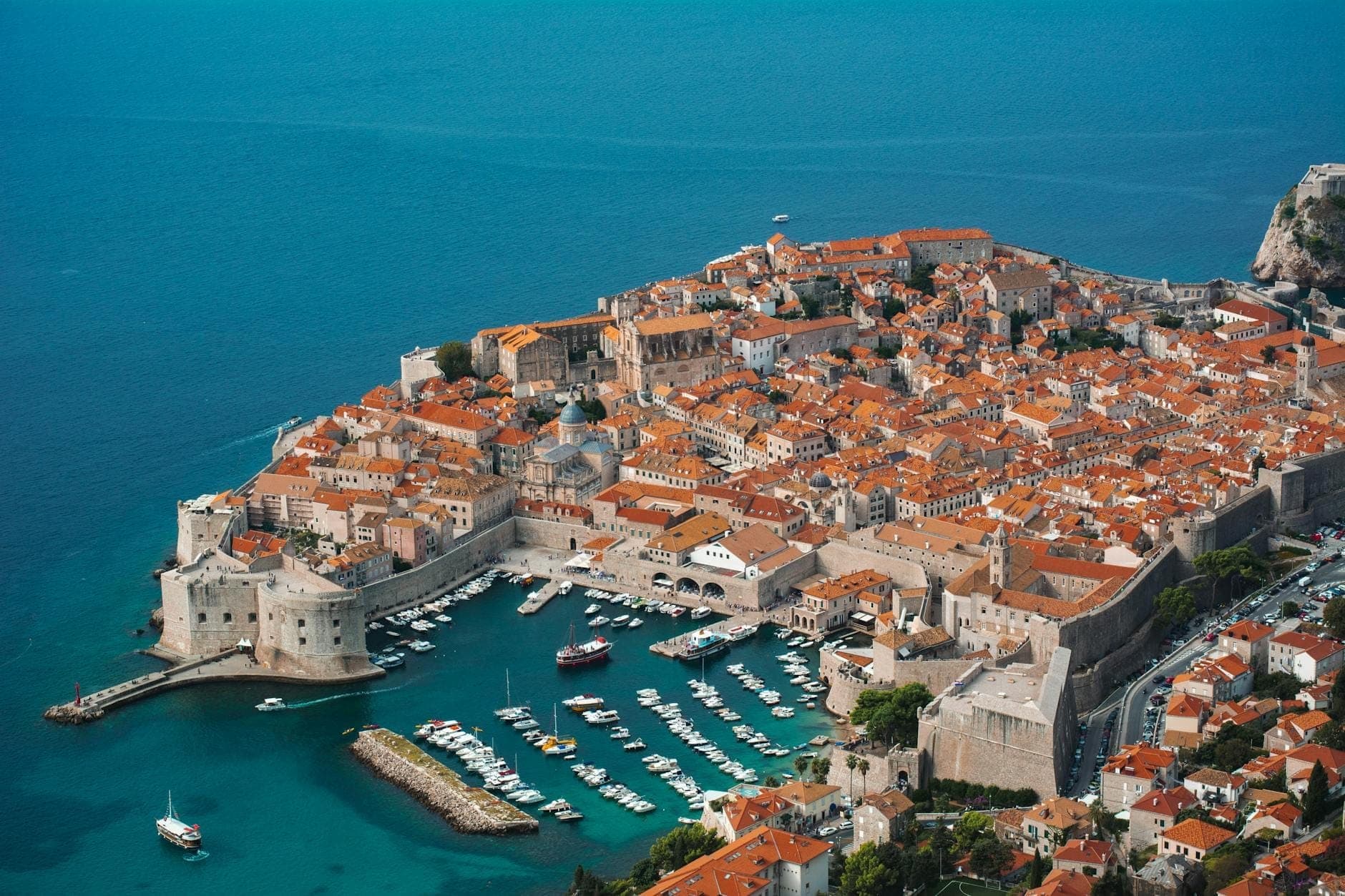 Pemandangan udara Kota Tua Dubrovnik yang bertembok dan marina yang dikelilingi oleh Laut Adriatik biru cerah pada hari yang cerah.