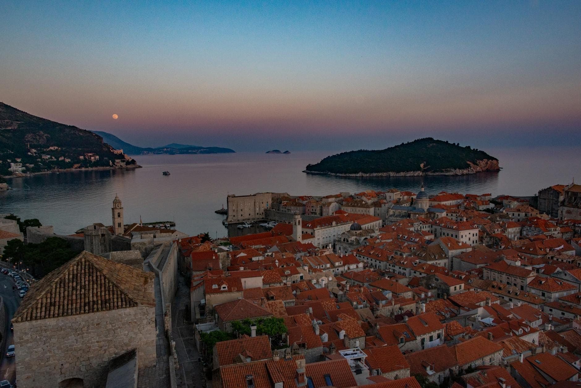 Vista panorámica del casco antiguo de Dubrovnik al atardecer, con tejados iluminados, murallas de la ciudad y el mar Adriático rodeando la península.