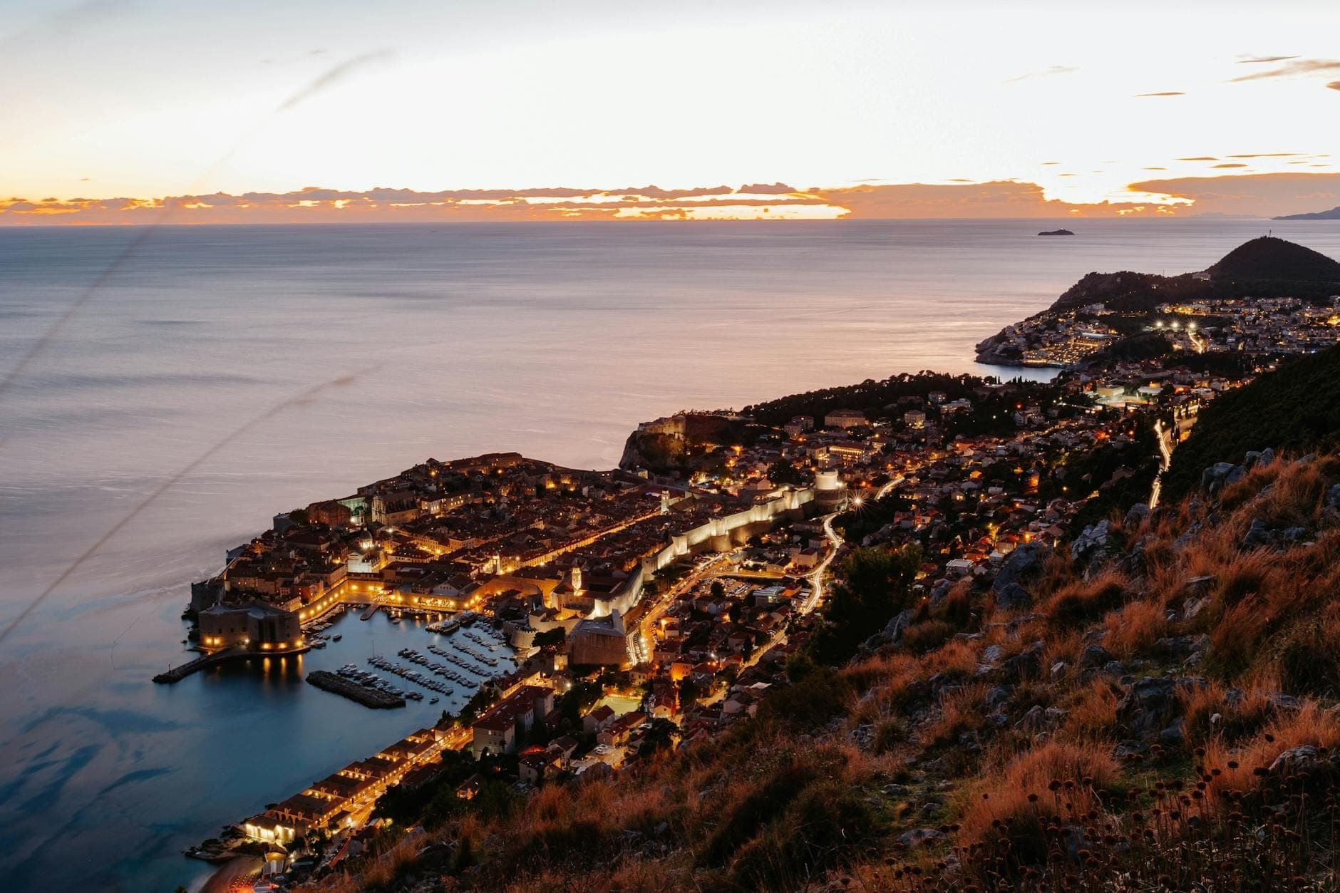 Beeindruckende Vogelperspektive auf Dubrovnik bei Sonnenuntergang – die beleuchteten alten Stadtmauern und die Adria im Hintergrund.