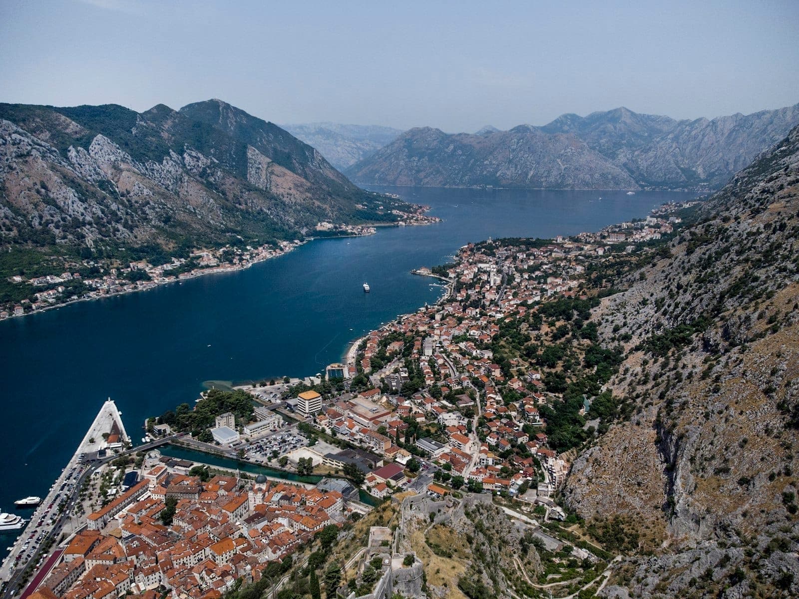 Une vue aérienne spectaculaire de la ville de Kotor, de la baie et des montagnes environnantes sous un ciel dégagé, mettant en valeur les paysages semblables à un fjord.