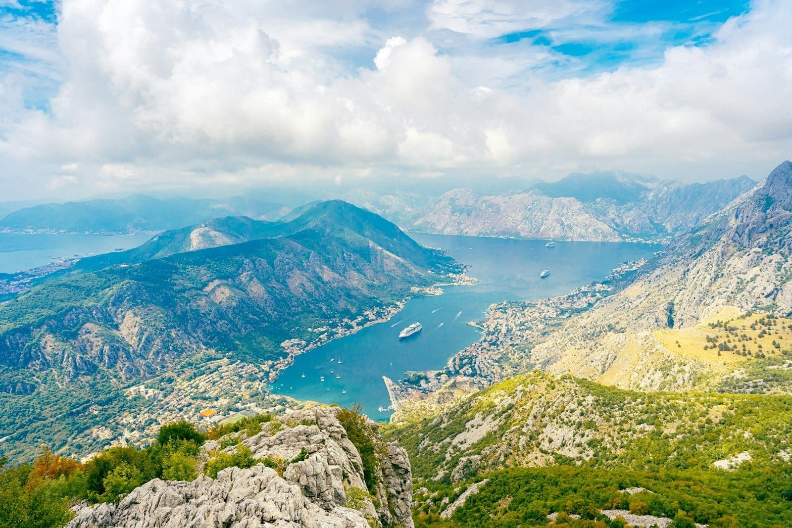 Vue panoramique de la Baie de Kotor avec route côtière sinueuse, montagnes et paquebots de croisière dans la baie.