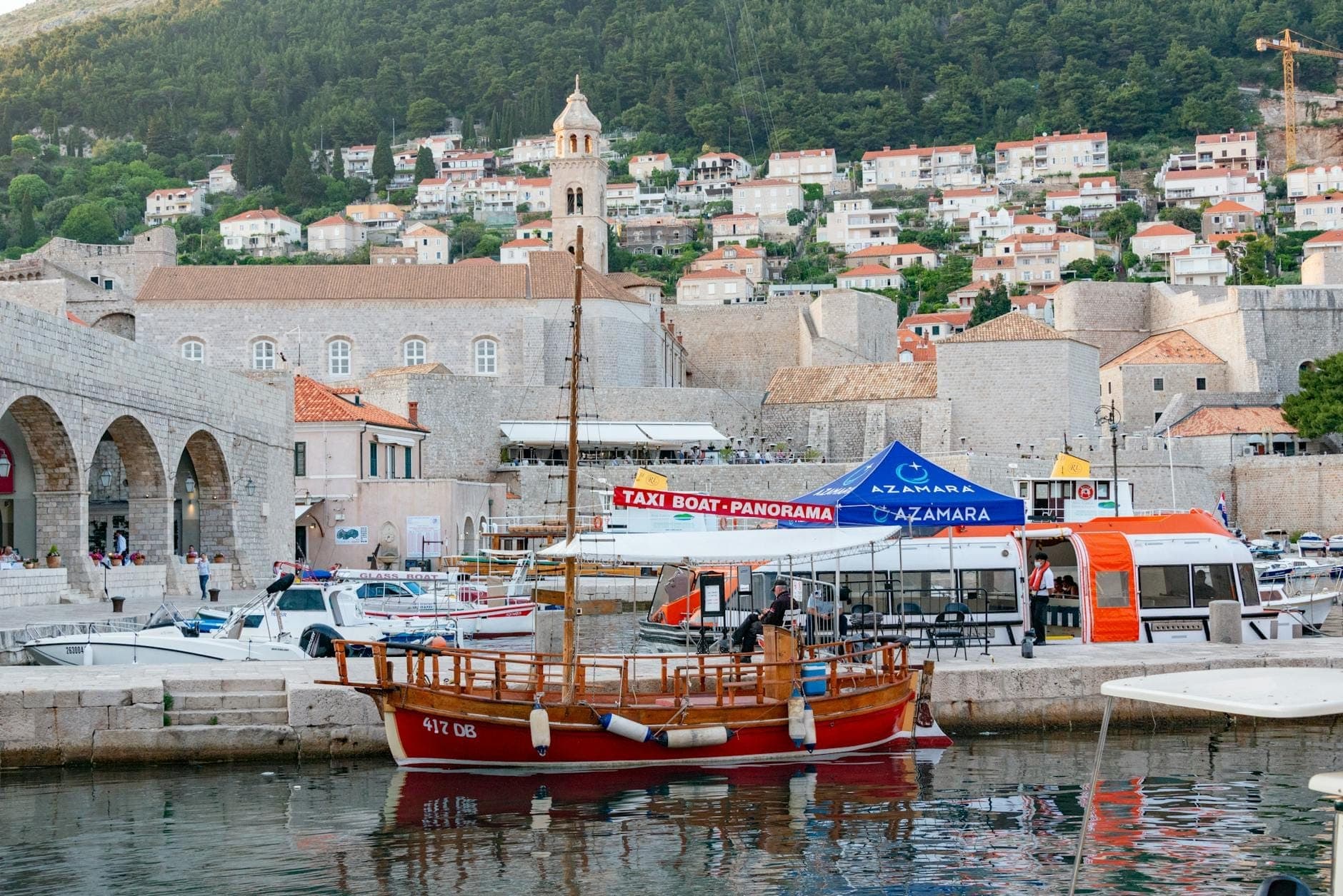 Porto de Dubrovnik com barcos, uma placa visível de táxi aquático e muralhas da cidade ao fundo, mostrando opções de transporte local.