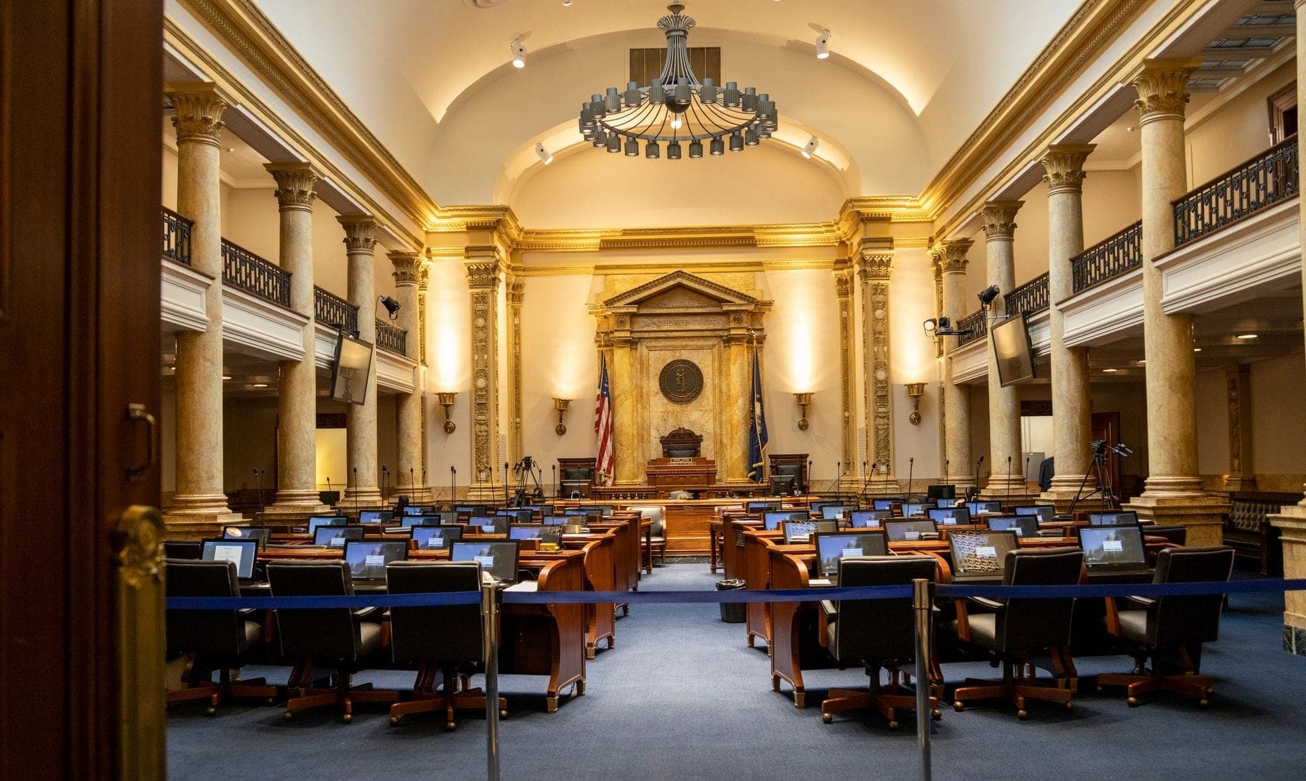 Vaste et élégante salle législative avec des bureaux et des chaises, des colonnes classiques, un plafond haut et des drapeaux américains, évoquant la salle du Sénat des États-Unis.