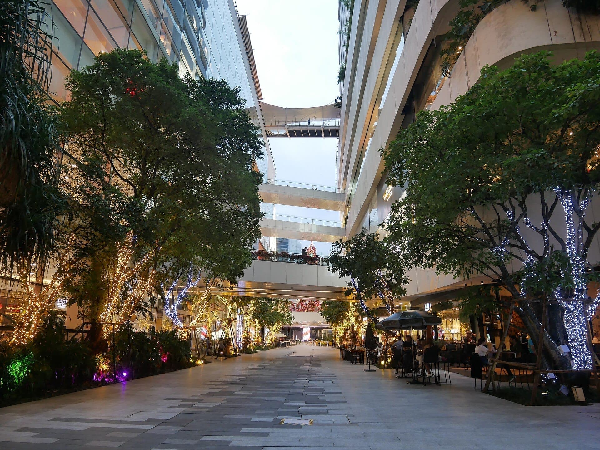 Le centre commercial EmQuartier à Bangkok avec sa passerelle en plein air, sa végétation luxuriante et ses terrasses sur plusieurs niveaux au crépuscule