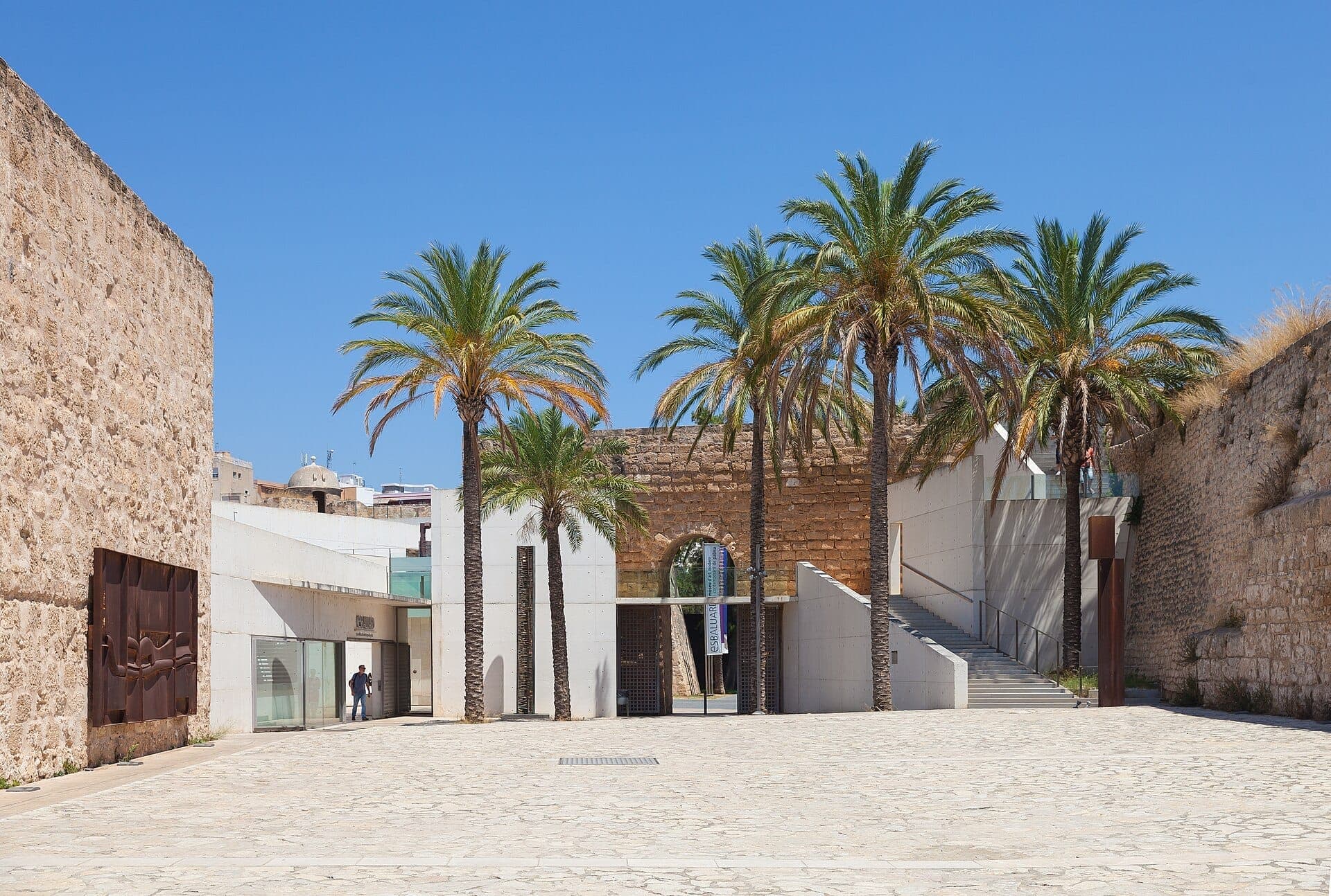 Eingangshof des Museums Es Baluard in Palma, mit Steinmauern, moderner Architektur, Palmen und klarem blauem Himmel.