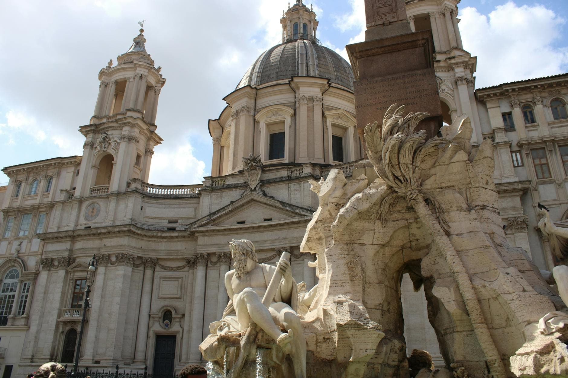Malawak na tanawin ng Fontana dei Quattro Fiumi na may mga dramatikong estatwa, dumadaloy na tubig, Ehipsiyong obelisko, at simbahang Sant'Agnese in Agone sa Piazza Navona.