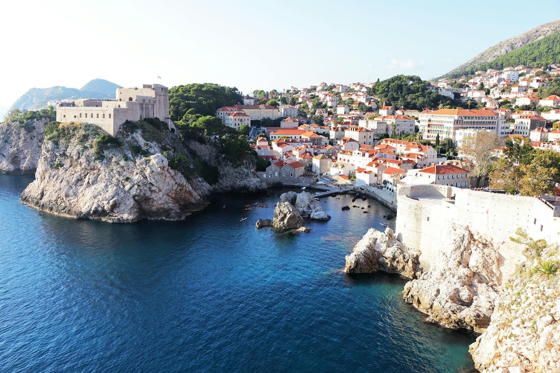 Weitwinkelansicht von Fort Lovrijenac auf einem felsigen Meereskliff mit Dubrovniks Altstadt und kristallblauem Wasser im Hintergrund an einem sonnigen Tag.