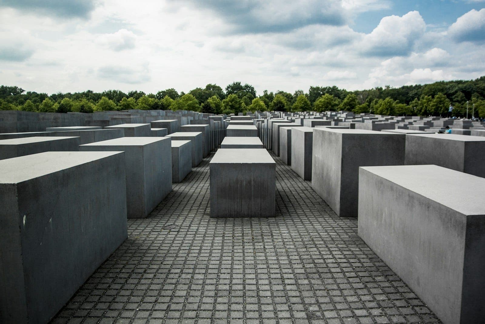 Vista ampia del Memoriale agli Ebrei Assassinati d'Europa a Berlino, con stele in cemento e alberi sullo sfondo sotto un cielo nuvoloso.