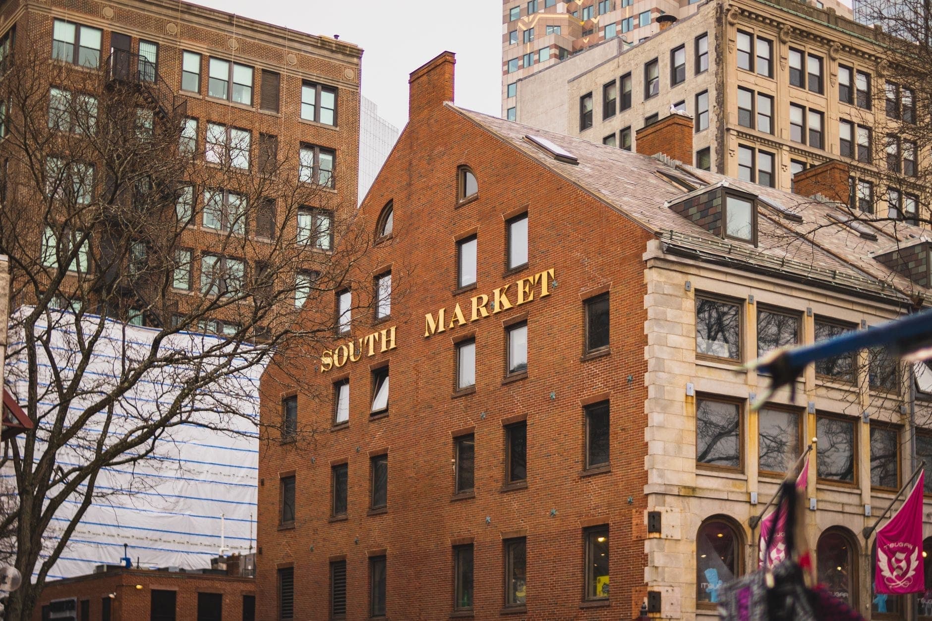 Bâtiment en brique avec de grandes lettres dorées indiquant 'South Market' au milieu de l'architecture du centre-ville de Boston par temps nuageux.