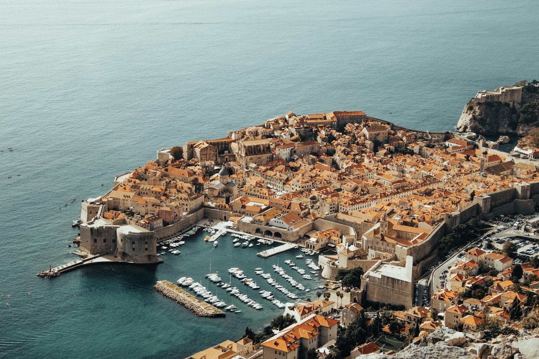 มุมมองทางอากาศของกำแพงป้อมปราการ ท่าเรือ และหลังคาสีส้มของเมืองเก่า Dubrovnik ที่เน้นสถาปัตยกรรมอันโดดเด่นซึ่งใช้เป็น King's Landing ใน Game of Thrones
