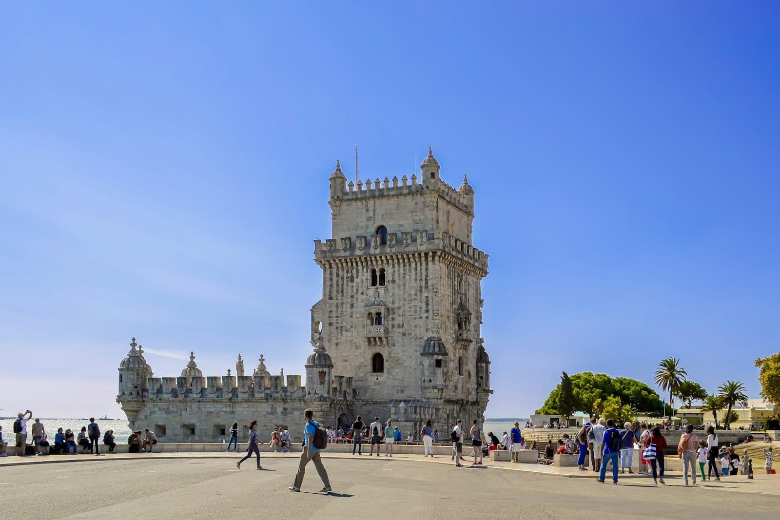 Turistas se reúnem na base da histórica Torre de Belém em Lisboa em um dia brilhante e ensolarado com céus azuis e limpos.