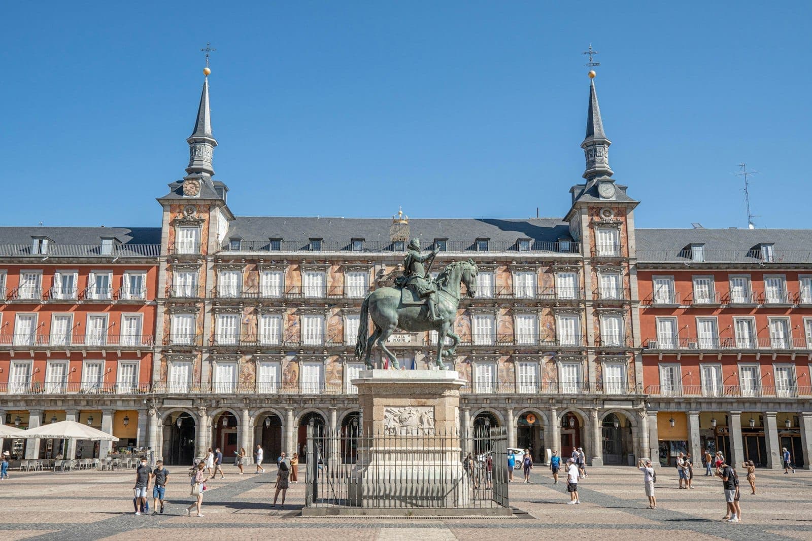 Vista panoramica di Plaza Mayor a Madrid con i suoi storici edifici rossi, la statua equestre centrale e persone che passeggiano in una giornata di sole