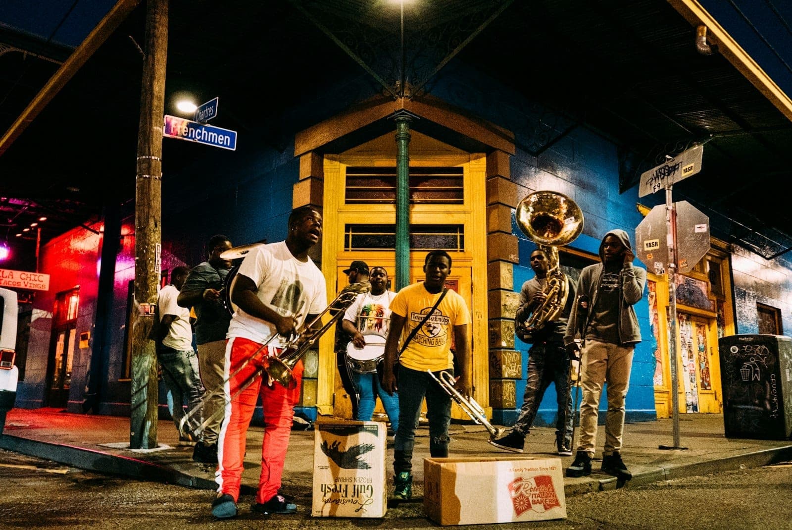 Żywa orkiestra dęta grająca nocą na słynnym rogu ulicy w New Orleans pod tabliczkami z nazwami ulic, z kolorowymi budynkami w tle.