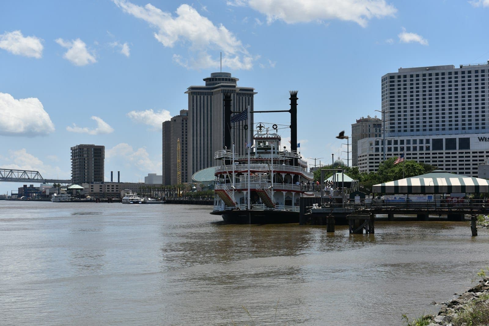 Parowiec zacumowany wzdłuż rzeki Mississippi z widoczną panoramą New Orleans i nabrzeżem w słoneczny dzień.