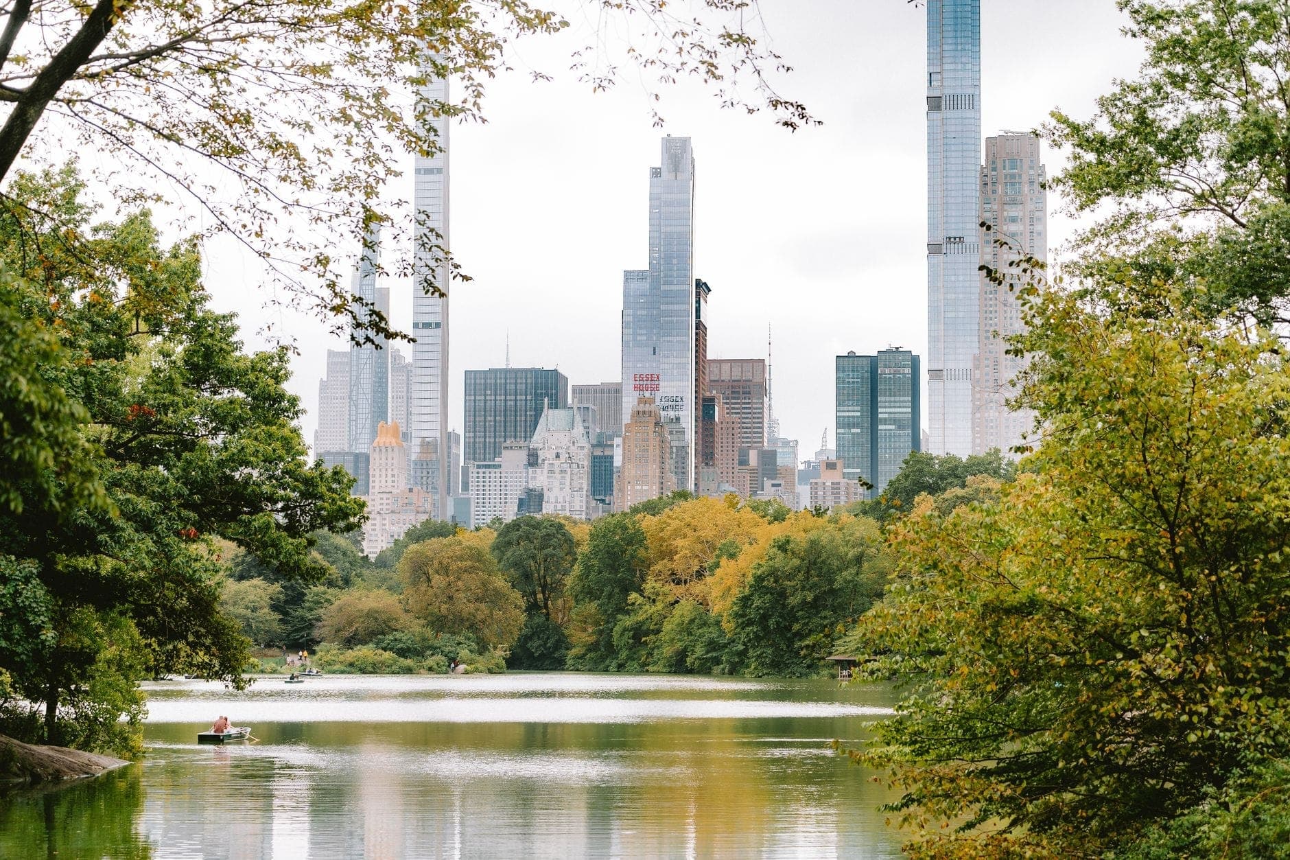 วิวทะเลสาบของ Central Park พร้อมต้นไม้สีเขียวและตึกระฟ้าของ Manhattan เป็นฉากหลัง บันทึกพื้นที่กลางแจ้งของ NYC ในวันที่มีเมฆมาก
