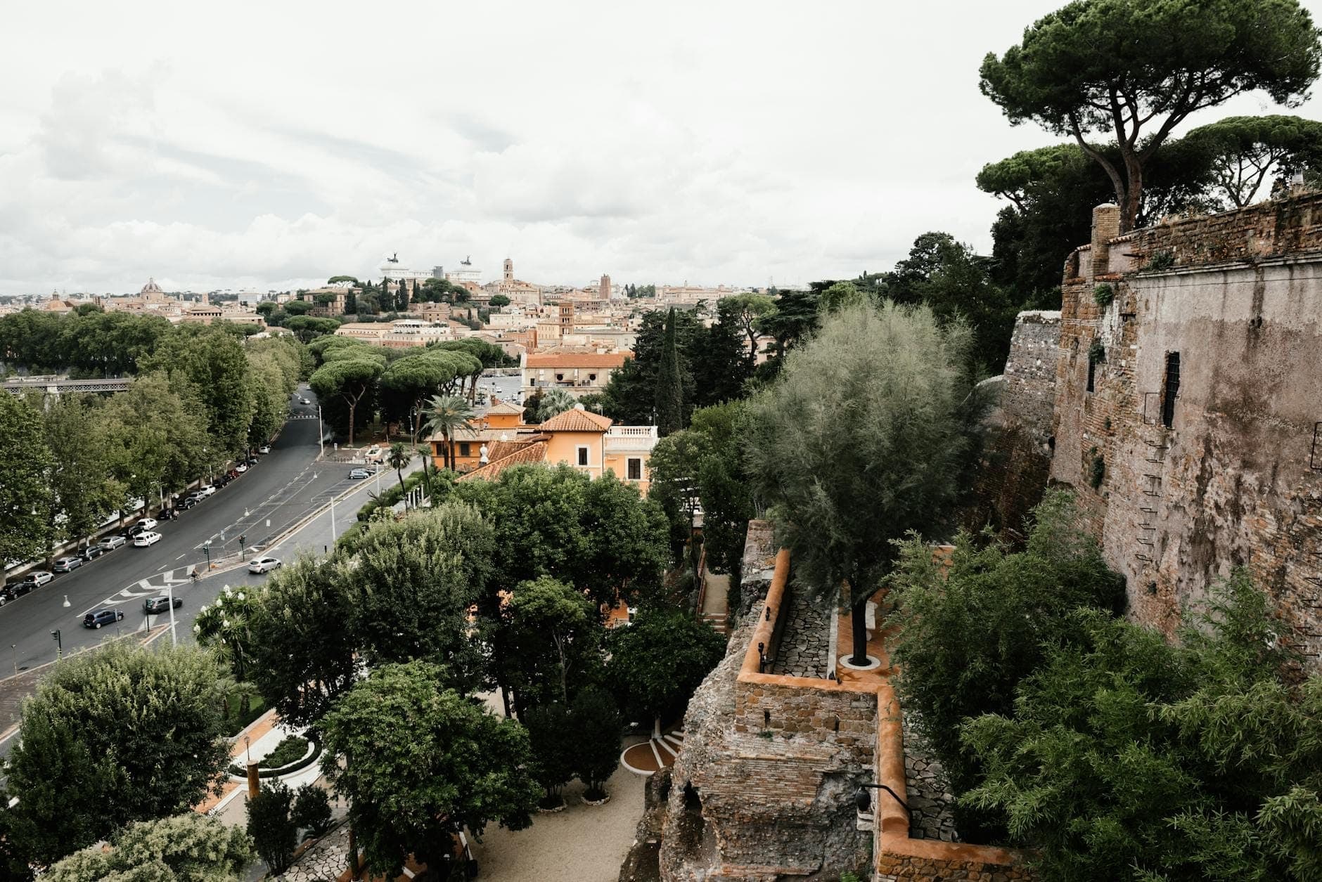 Vue depuis une colline à Rome avec le paysage urbain, des arbres, d'anciens murs en pierre et une route qui serpente à travers la verdure.