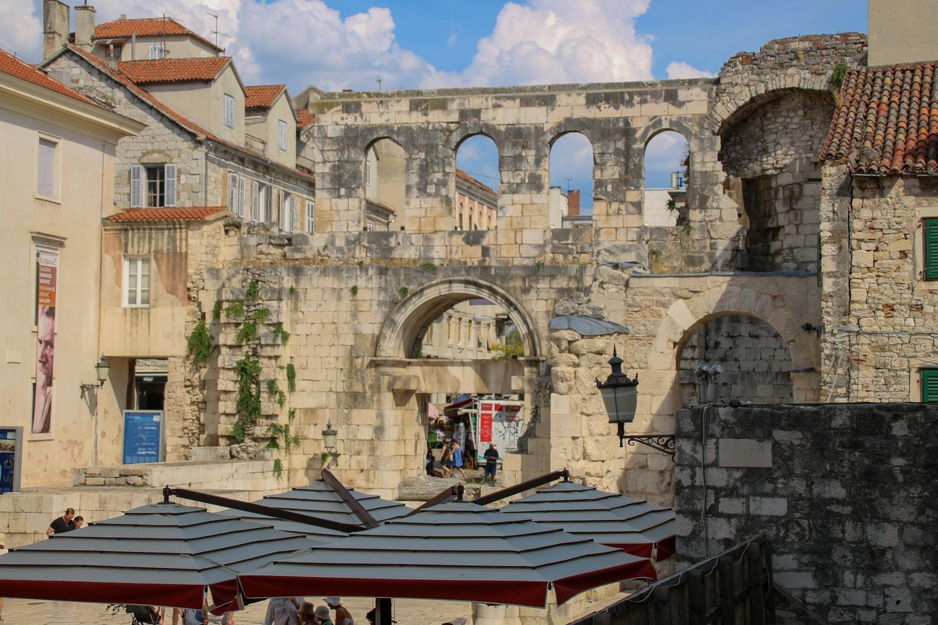 Ancienne porte en pierre avec des arches et des ruines romaines dans la vieille ville de Split, en Croatie, entourée de bâtiments historiques.