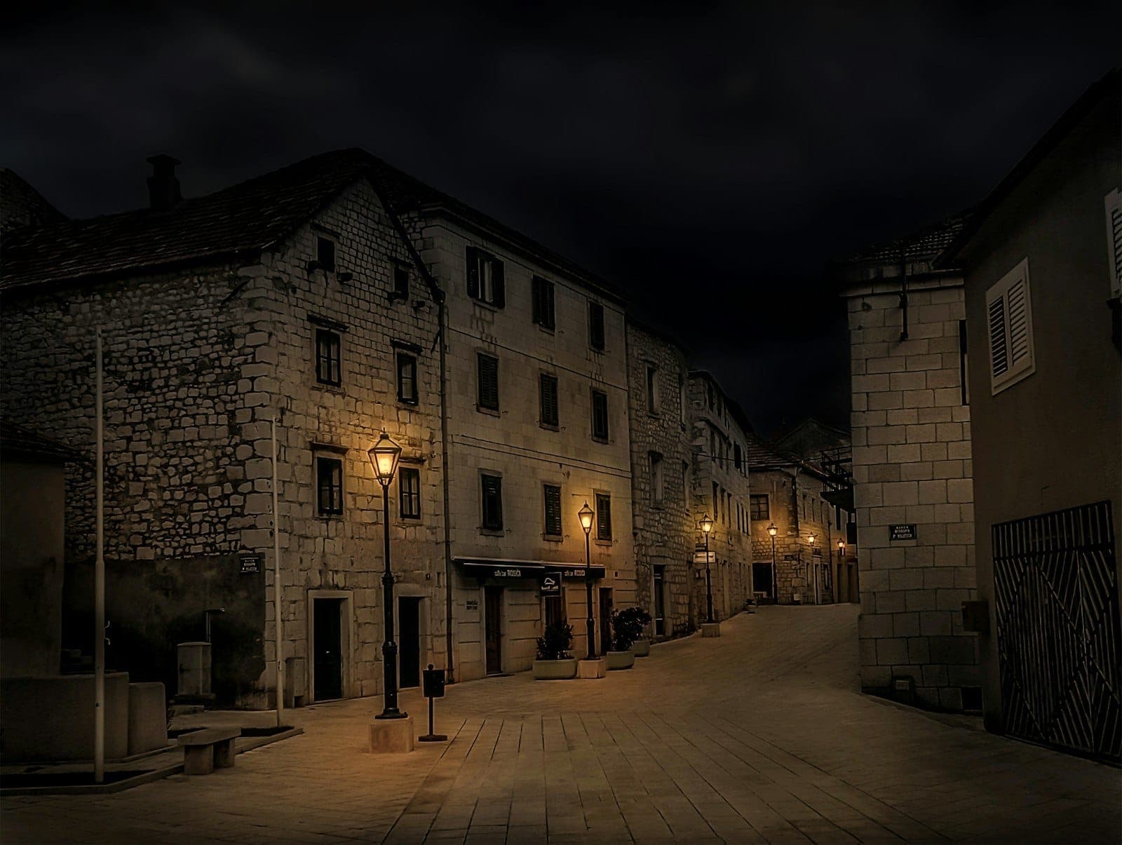 Ruelle en pierre déserte avec des bâtiments historiques à Split la nuit, illuminée par des lanternes à l'ancienne.