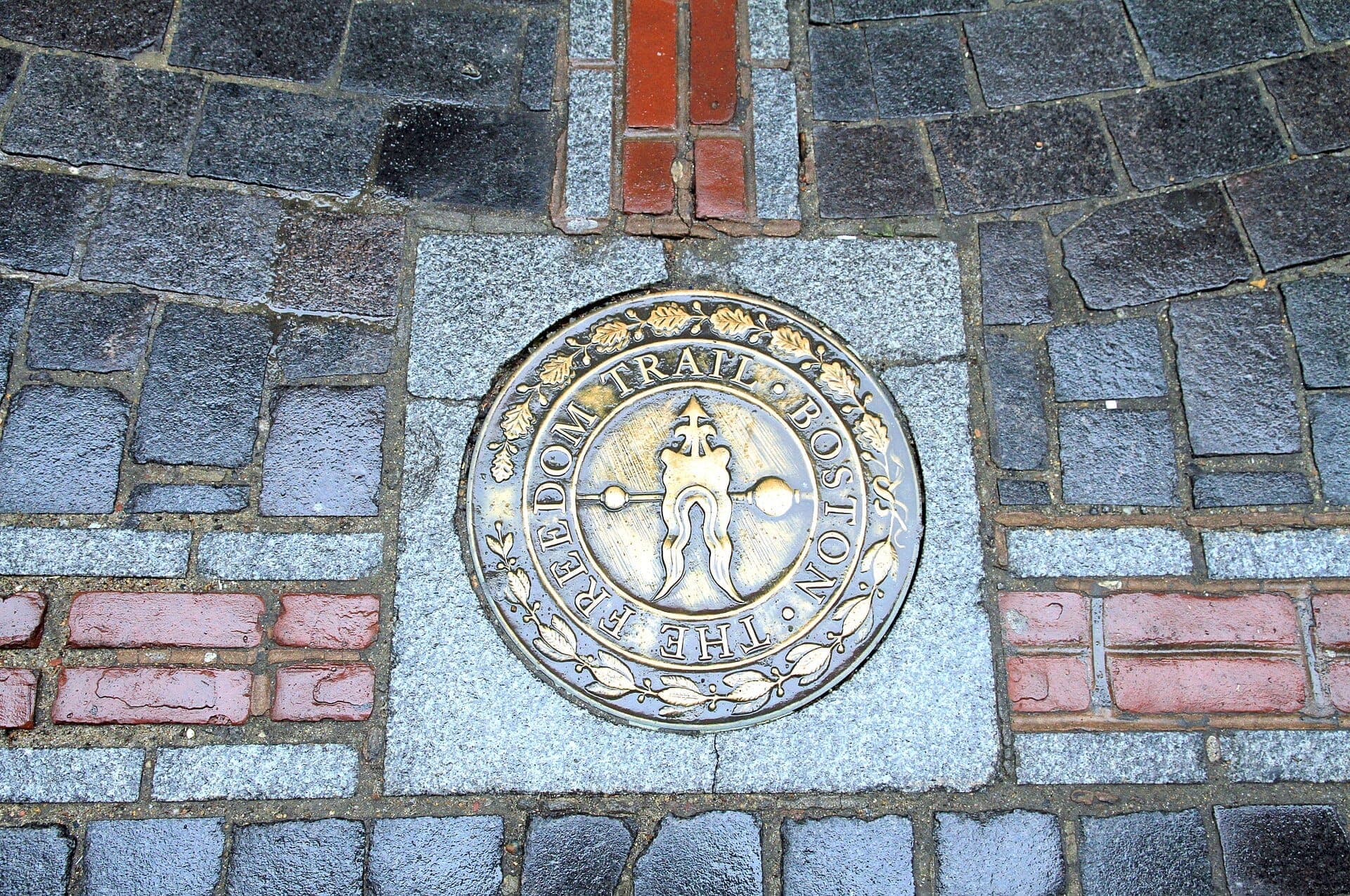 Gros plan du médaillon du Freedom Trail incrusté dans un trottoir pavé à Boston, avec des briques rouges et des pierres grises visibles autour.