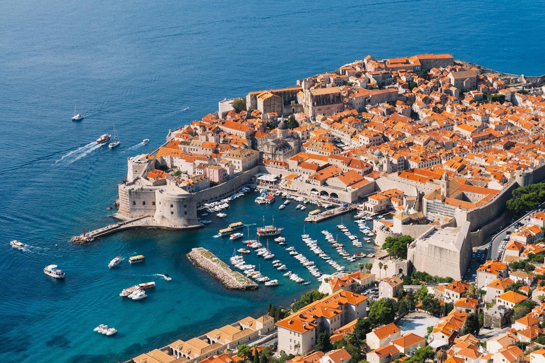 Dramatische Luftaufnahme von Dubrovniks Altstadtmauern, Festungen, orangefarbenen Dächern und dem Hafen am leuchtend blauen Adriatischen Meer.
