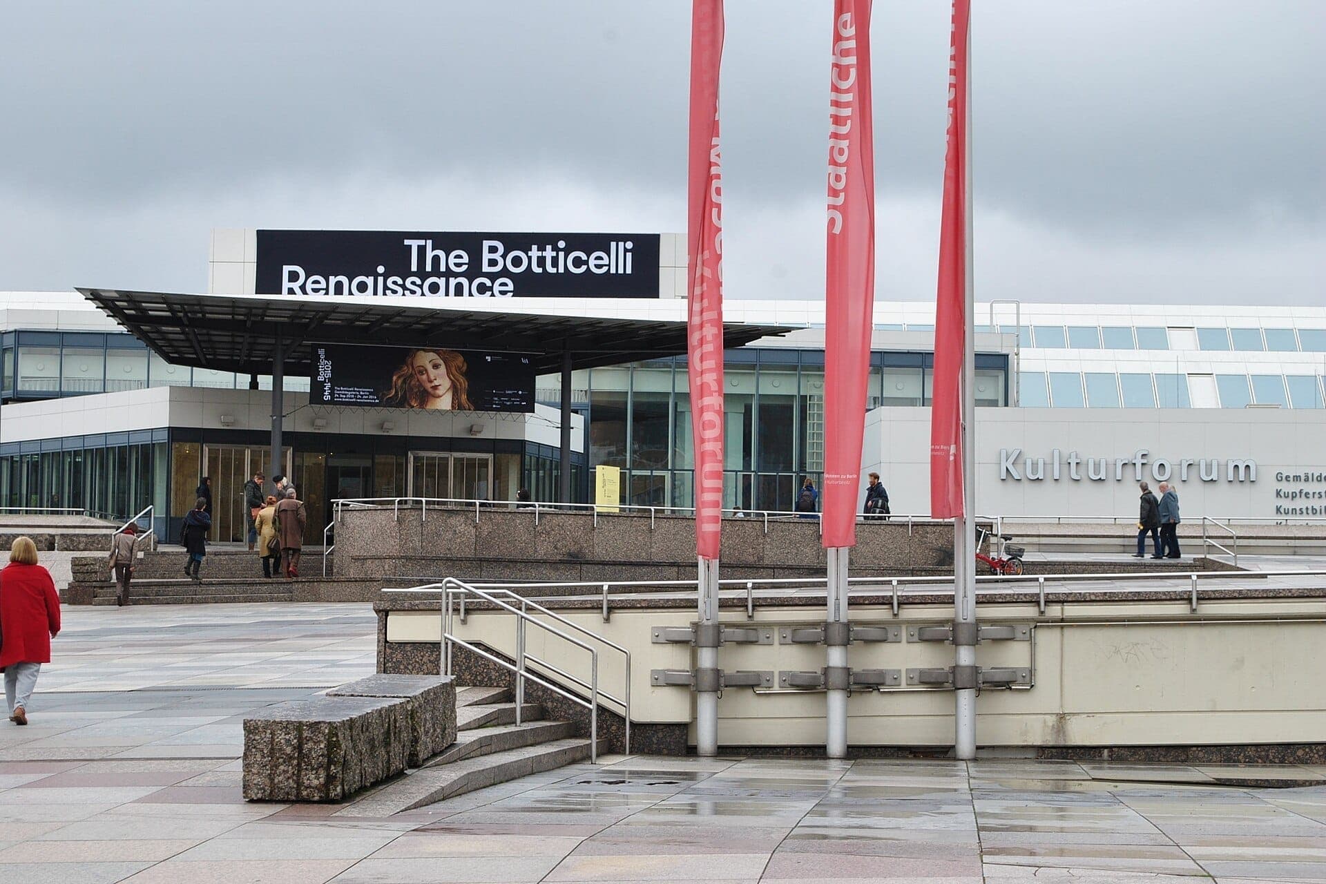 วิวภายนอกของ Gemäldegalerie Berlin ที่ Kulturforum พร้อมสถาปัตยกรรมสมัยใหม่ หน้าต่างกระจกขนาดใหญ่ ธงสีแดง และผู้คนที่เดินผ่านบริเวณทางเข้า