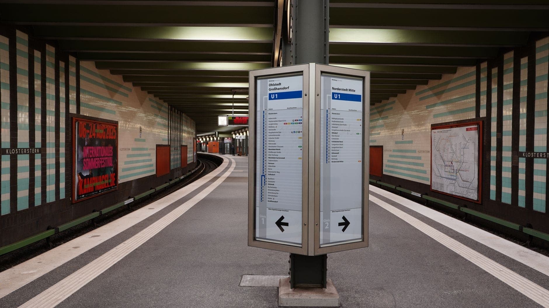 ชานชาลา U-Bahn ในเบอร์ลินพร้อมป้ายข้อมูลเส้นทาง ป้ายตารางเวลา และผนังสถานีที่ปูด้วยกระเบื้อง แสดงให้เห็นระบบขนส่งสาธารณะในท้องถิ่น