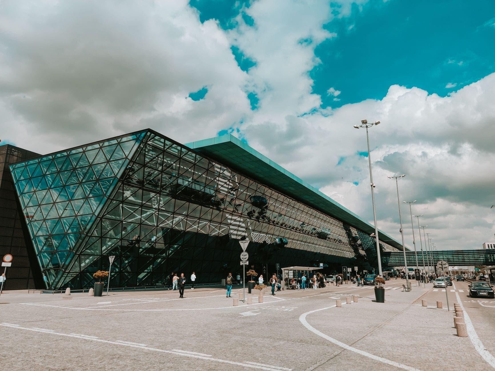 ด้านหน้ากระจกสมัยใหม่ของสนามบิน Berlin Brandenburg พร้อมนักเดินทางและยานพาหนะด้านหน้าในวันที่มีเมฆบางส่วน