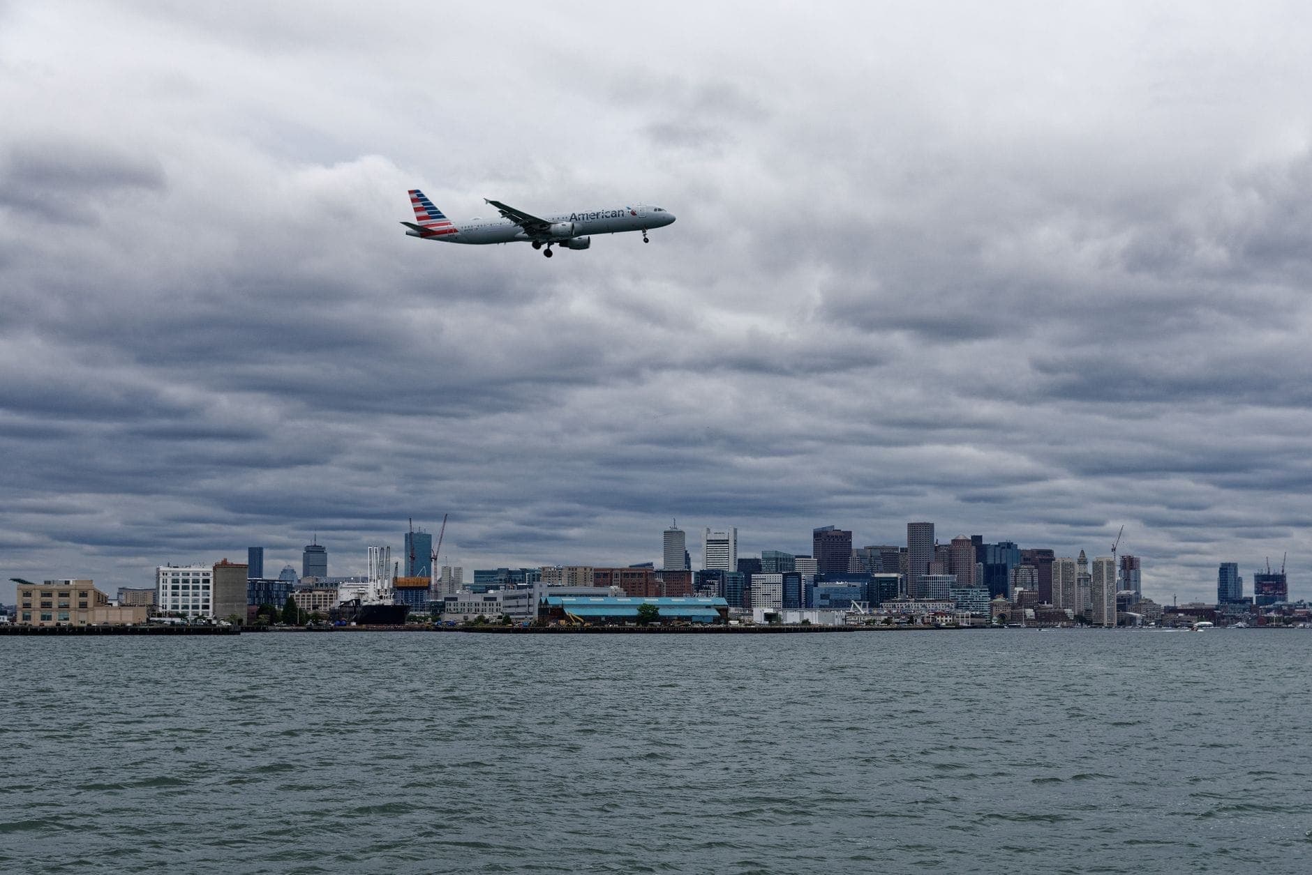 Avion atterrissant au-dessus de Boston Harbor avec la skyline de Boston en arrière-plan par un jour nuageux.