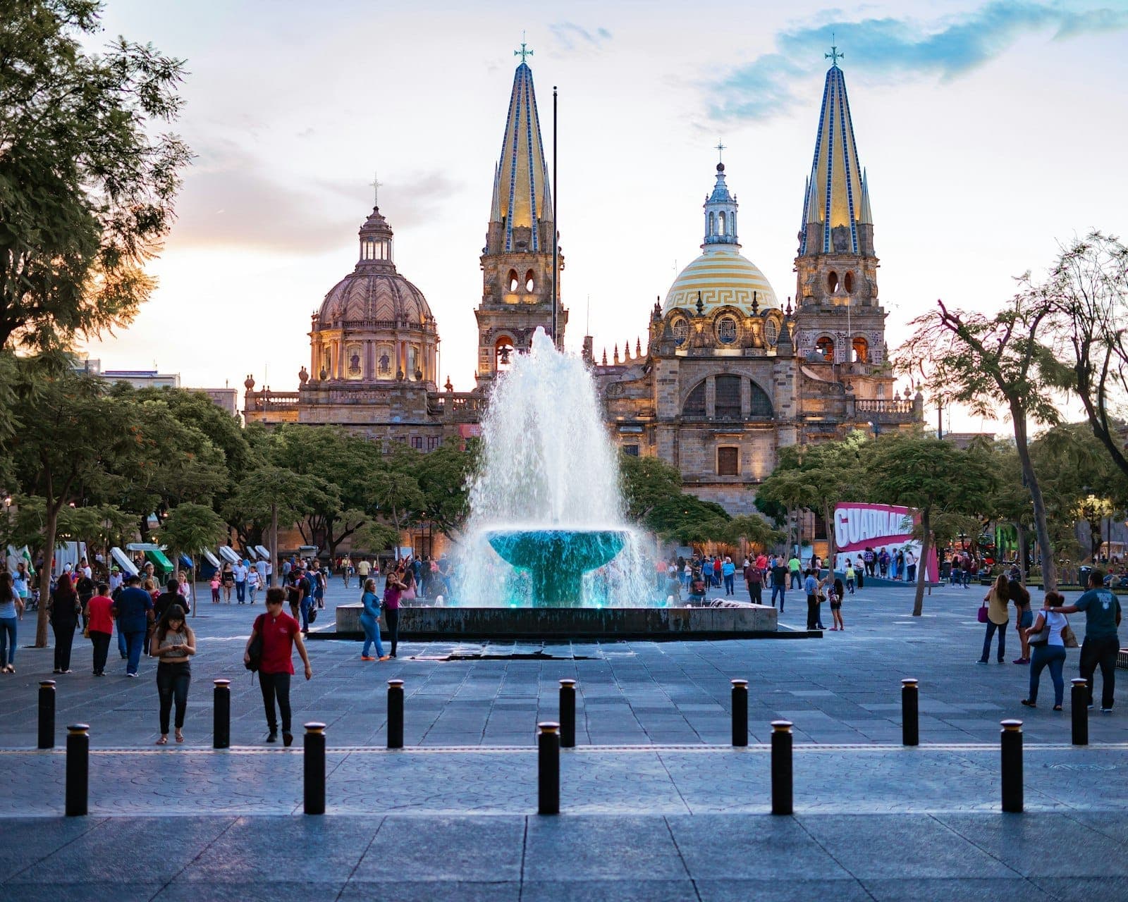 ผู้คนเดินผ่านจัตุรัสที่คึกคักพร้อมน้ำพุและมหาวิหาร Guadalajara ในพื้นหลังช่วงพระอาทิตย์ตก