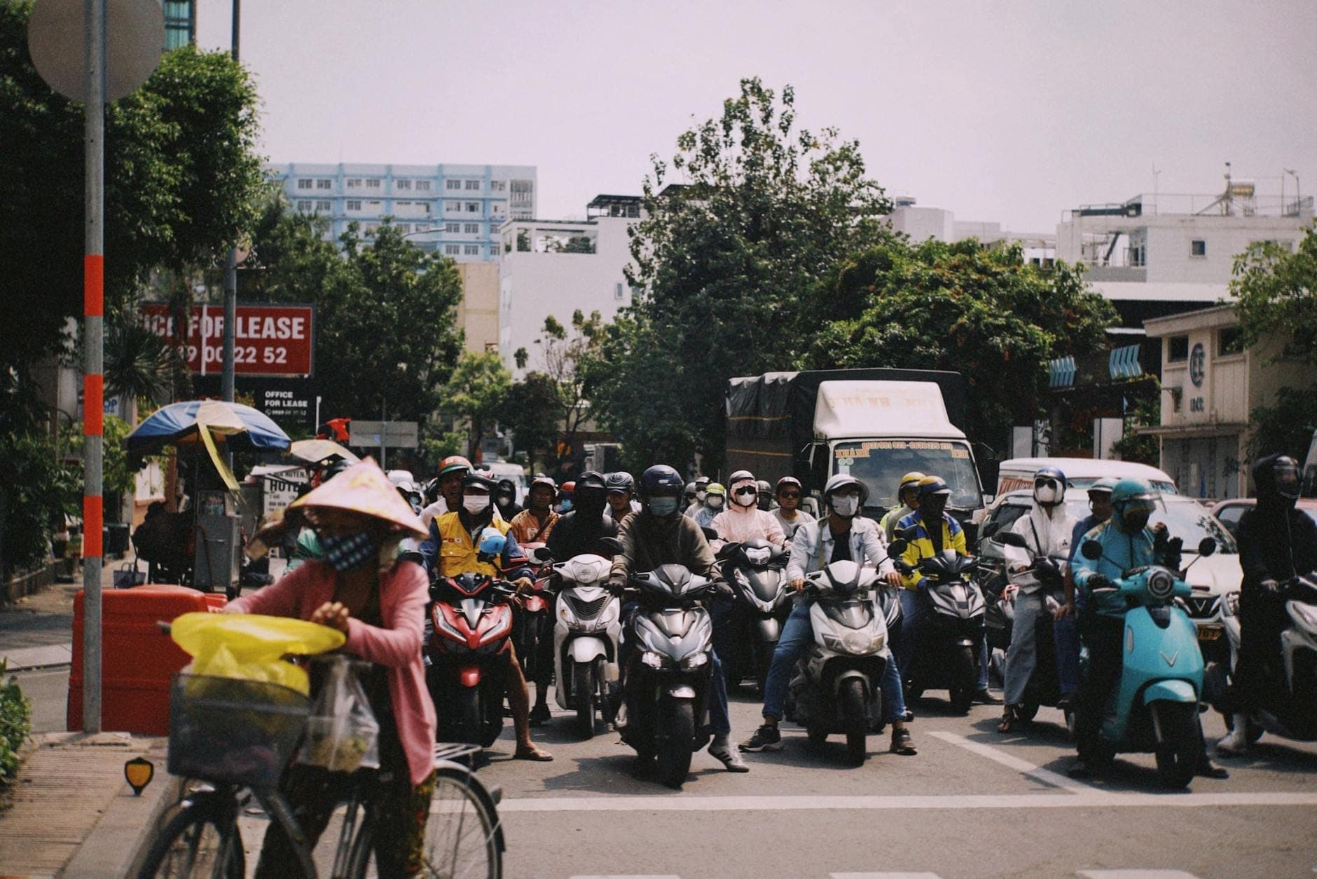 Busy Ho Chi Minh City intersection with many motorbikes and a person cycling in the foreground at a crosswalk.