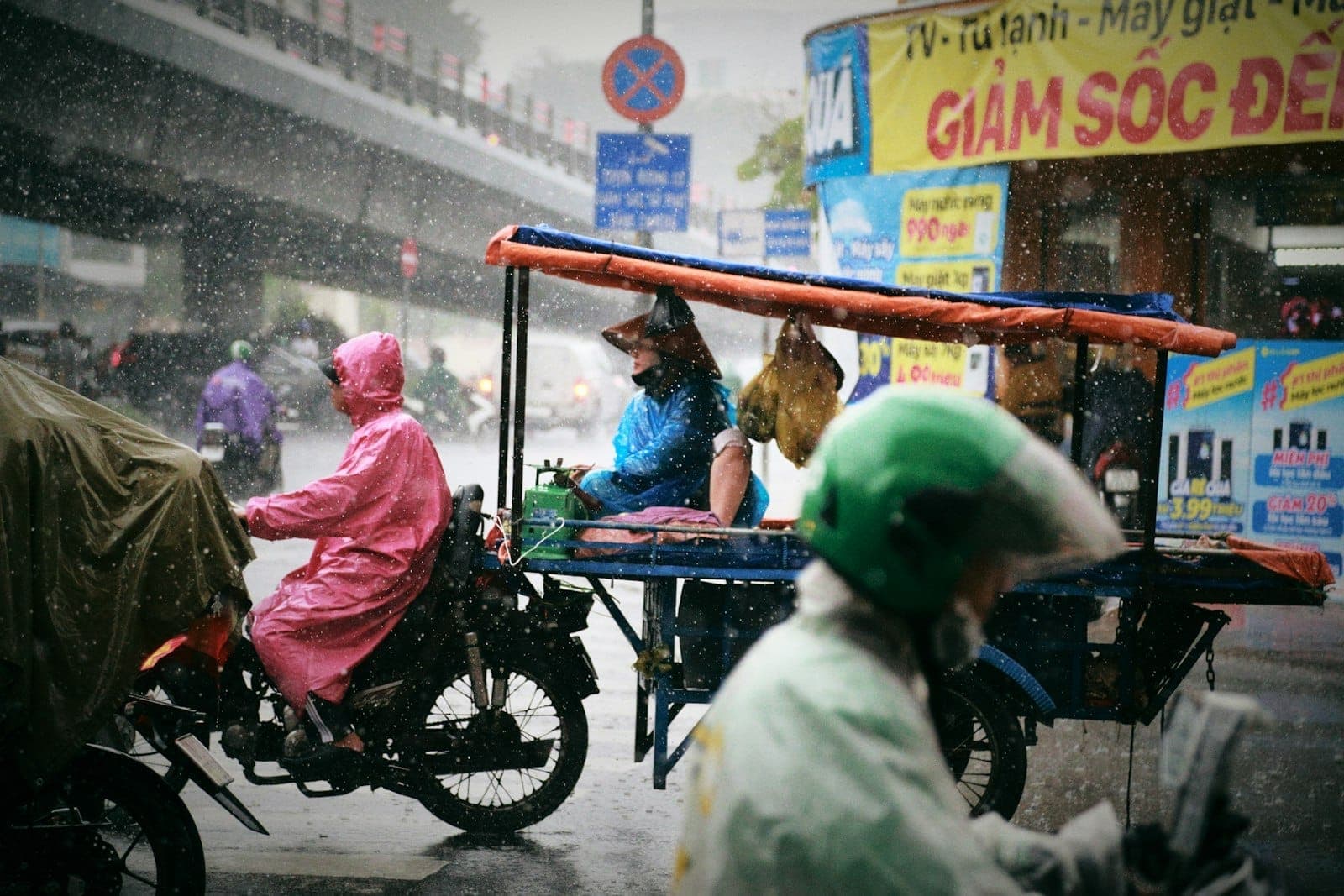Motorbikes and street vendors in Ho Chi Minh City during heavy rain, people wearing raincoats, and rain falling visibly.