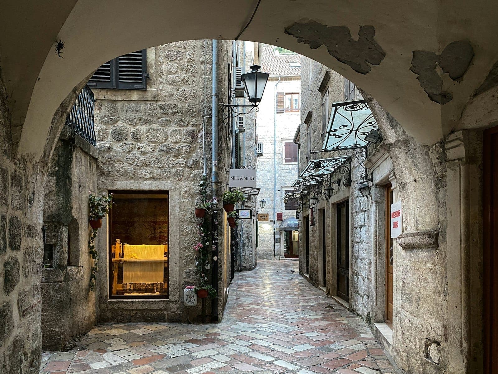 Ruelle étroite pavée de galets bordée de vieux bâtiments en pierre et d'arches dans la vieille ville de Kotor, Monténégro.