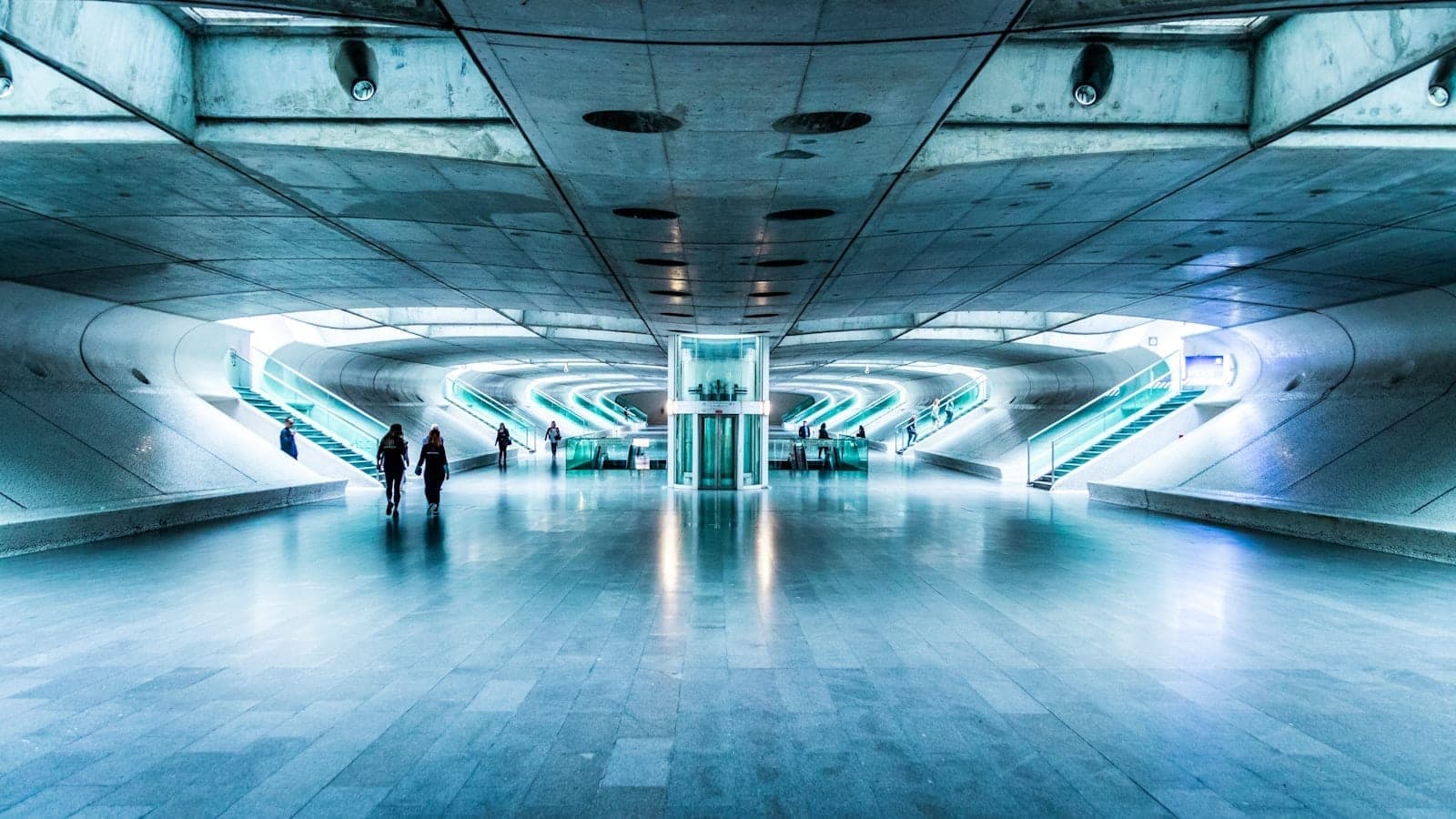 Vista ampla de uma estação de metrô moderna e bem iluminada em Lisboa com escadas rolantes e design futurista, poucas pessoas caminhando no interior.