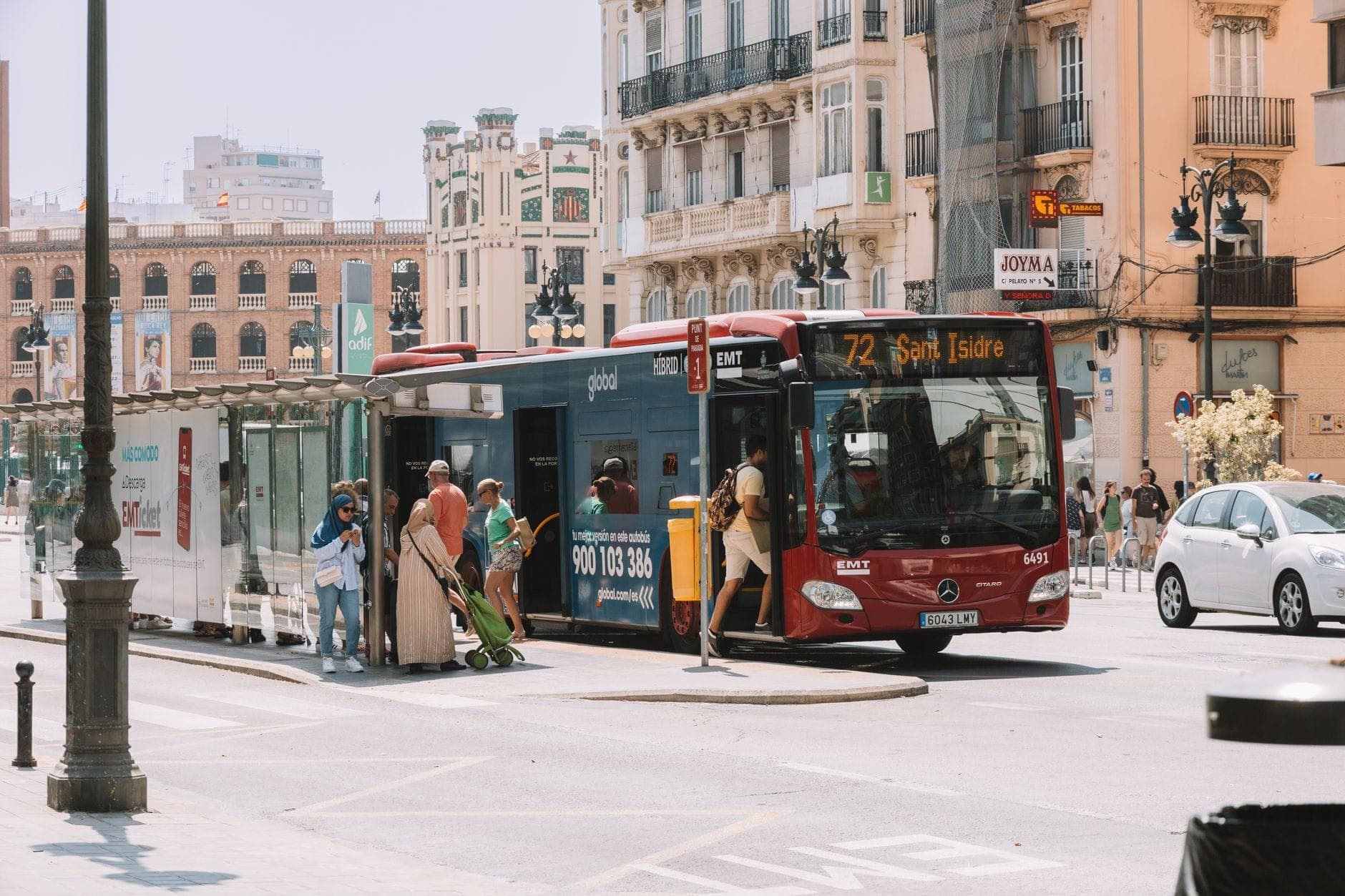 Autobús rojo de la EMT Madrid con pasajeros subiendo en una parada en una concurrida calle de Madrid, con edificios clásicos al fondo.