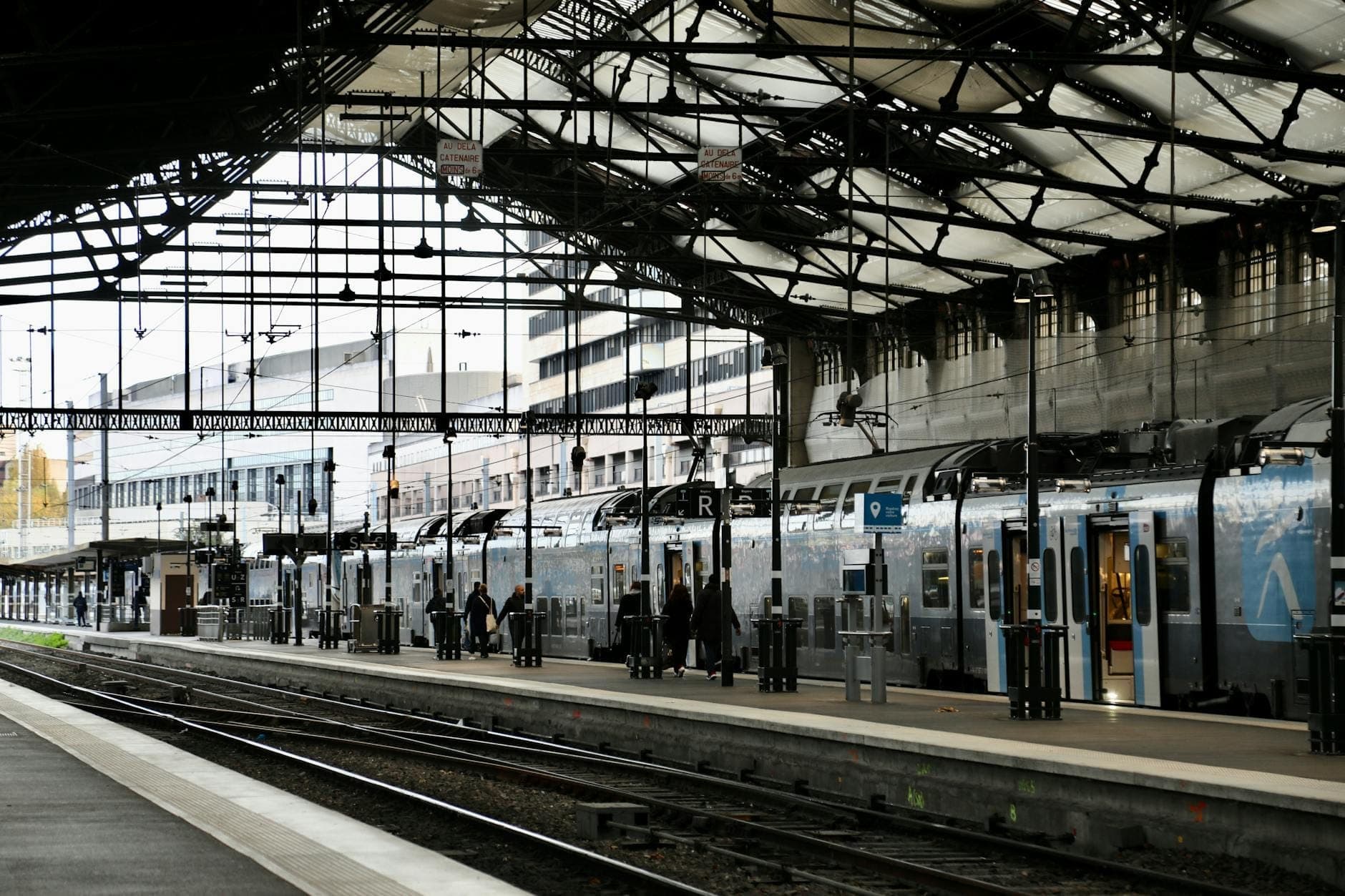 Covered platform at a Parisian railway station with people boarding a modern double-decker regional train.