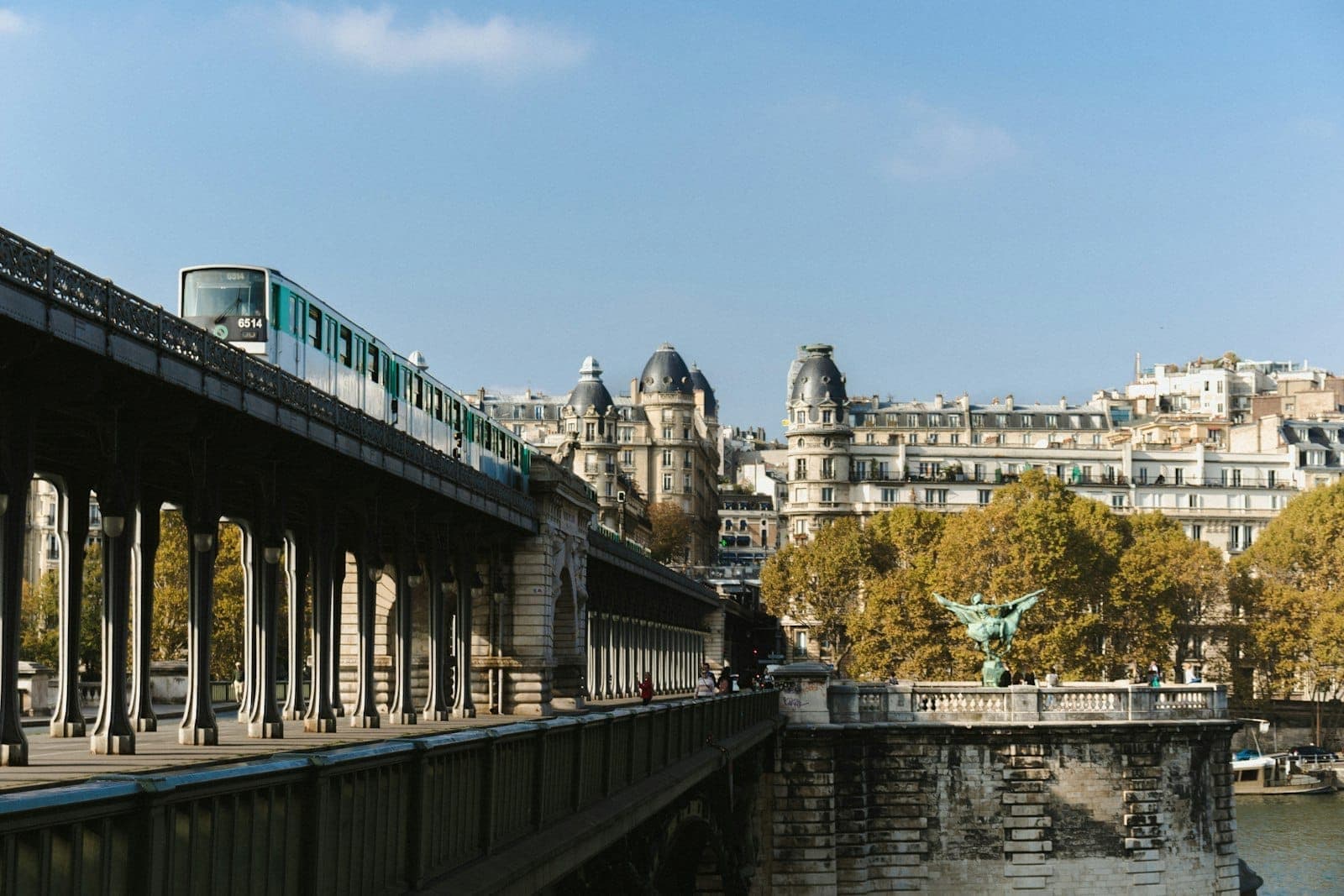 Paris Metro train crossing Bir-Hakeim bridge above the Seine with classic Parisian buildings and trees in the background on a clear day.