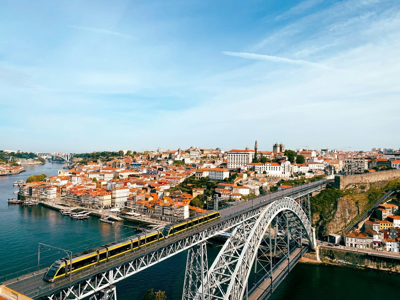 Una vista panoramica di Porto con l'iconica Ponte Dom Luís I, un treno della metropolitana giallo che attraversa il Douro e lo skyline storico della città al sole.