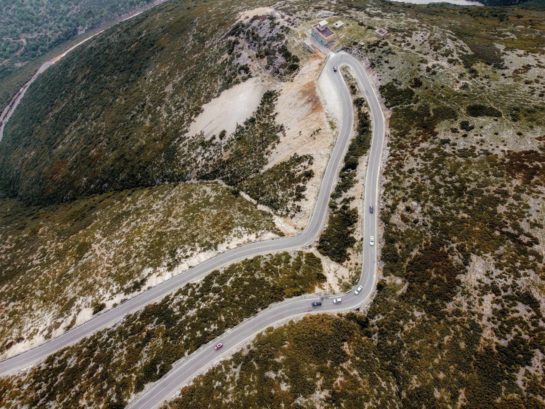 Vista aérea de una sinuosa carretera de montaña de dos carriles en Cerdeña con escaso tráfico y terreno accidentado a ambos lados.