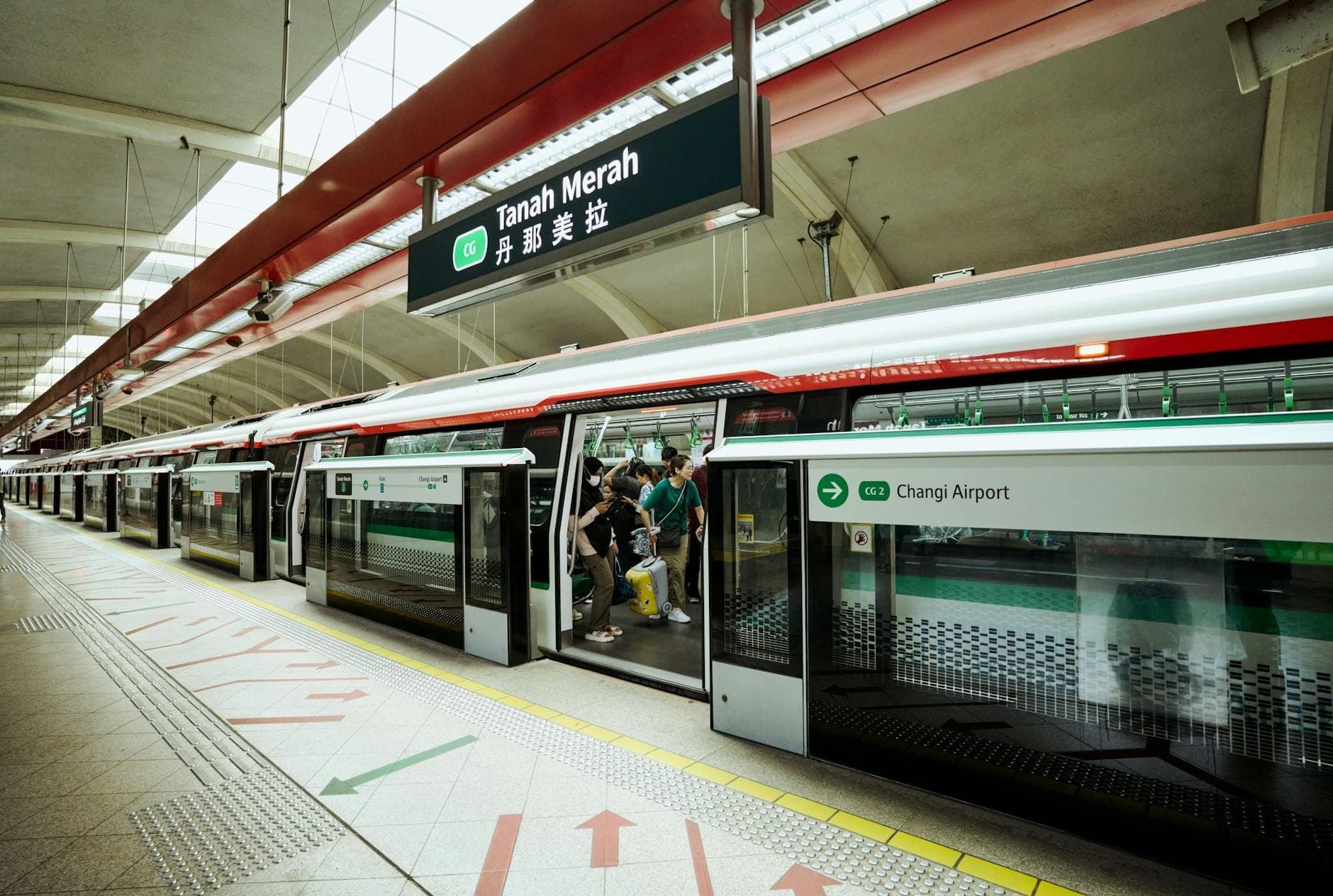 Bahnsteig der MRT-Station Tanah Merah in Singapur, mit geöffneten Zugtüren, einsteigenden Fahrgästen und gut sichtbarer MRT-Beschilderung.